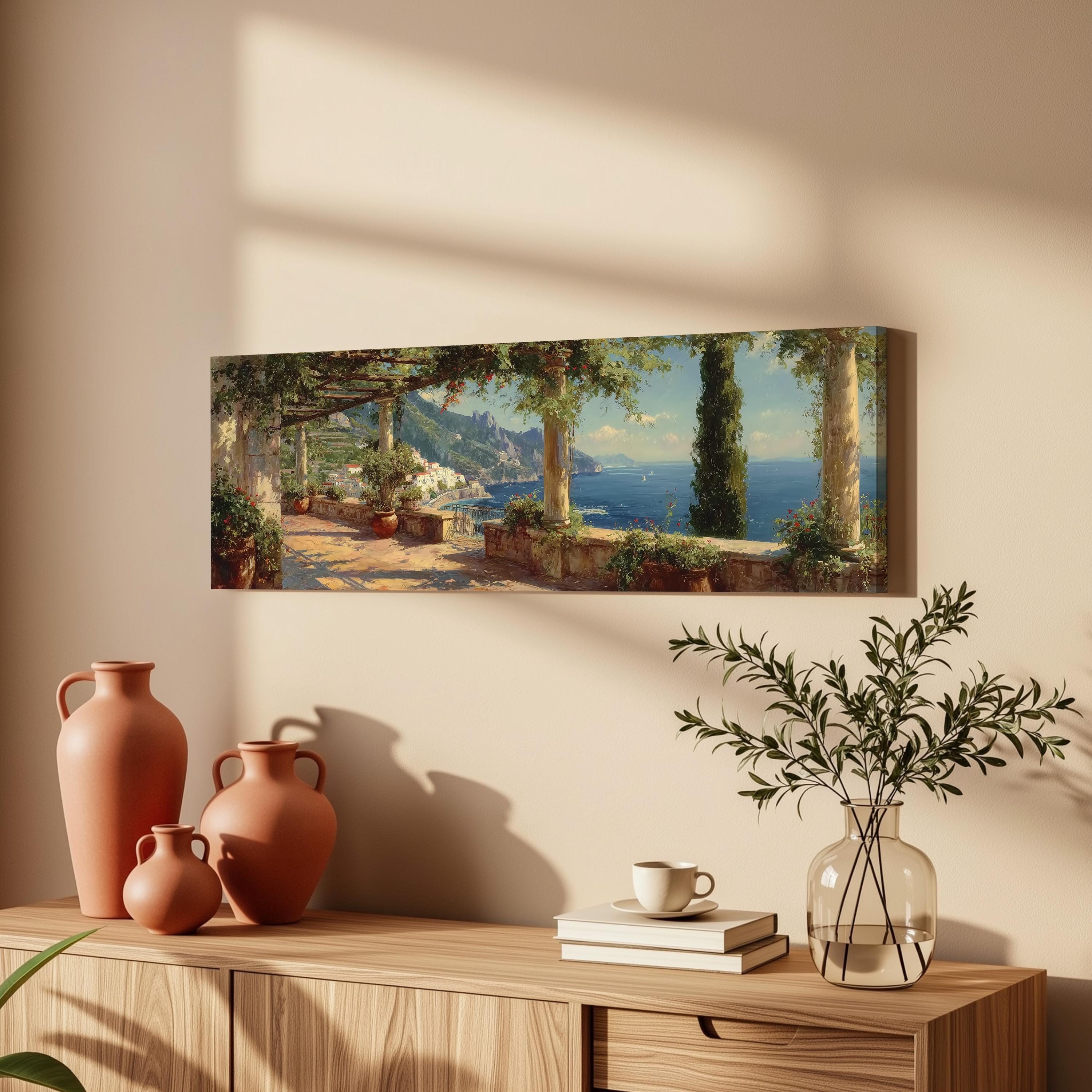 a serene coastal scene with a walkway lined with trees and potted plants, overlooking the ocean. The painting is hung on a wall above a wooden dresser, which has a vase, a coffee cup, and a stack of books on it.