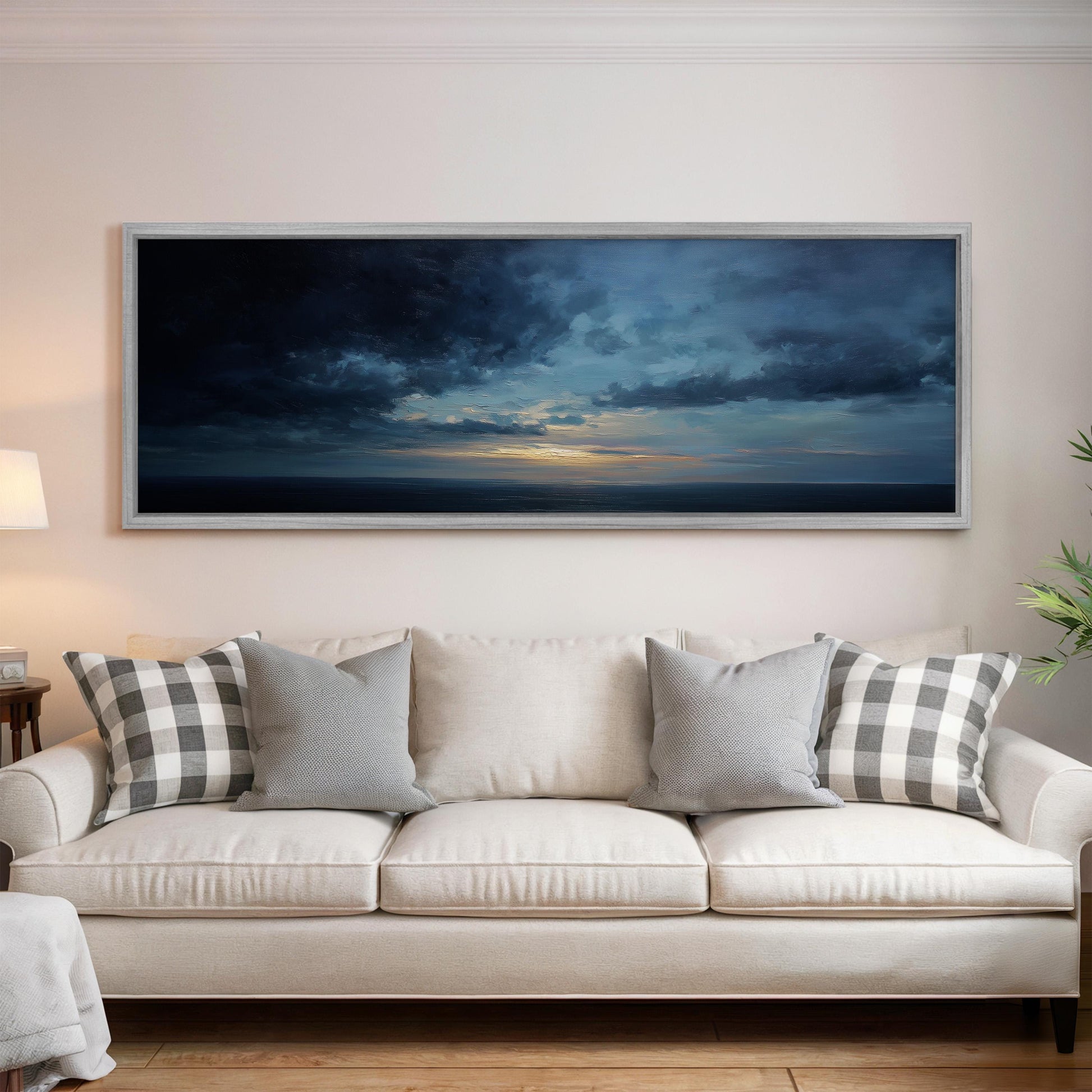 a large, framed painting of a dramatic sky with clouds hanging above a white couch with gray and white plaid throw pillows.