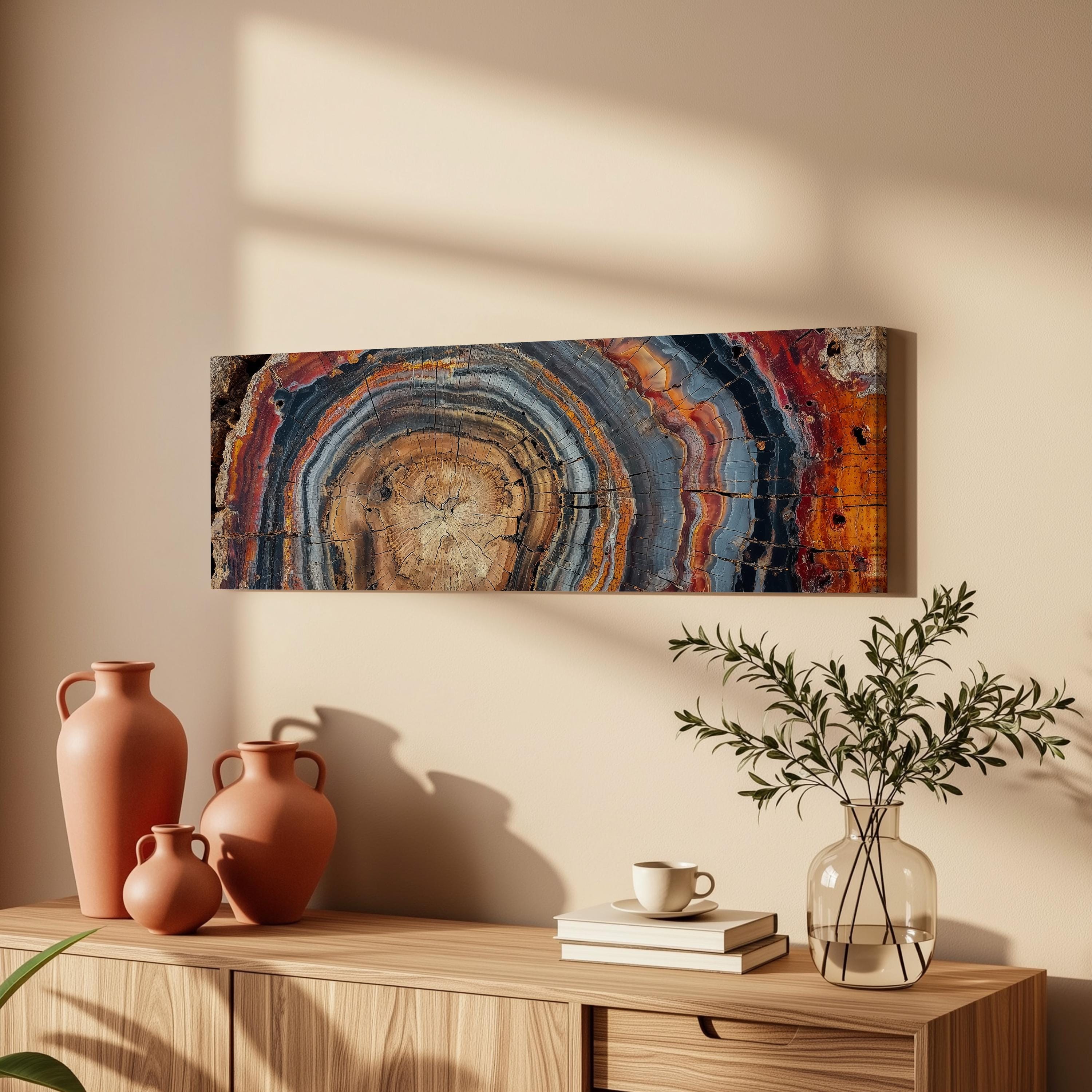 a wooden cabinet with a vase, a plant, and a stack of books on top. Above the cabinet, there is a large abstract painting hanging on the wall.