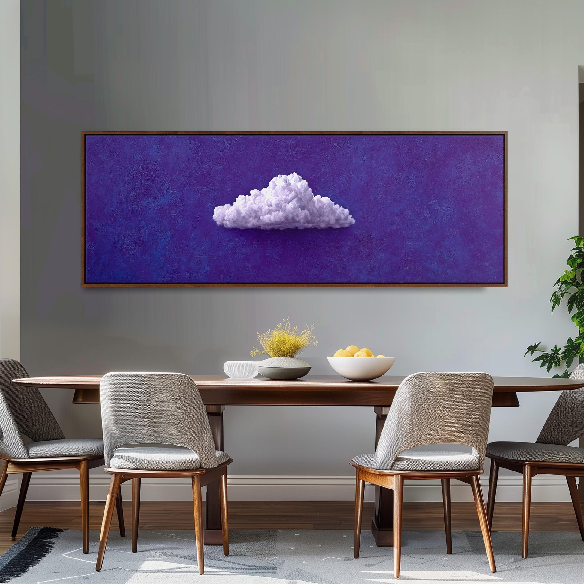 a dining room with a wooden table and four chairs. Above the table, there is a large painting of a cloud on a purple background. The table is set with a bowl of fruit and a vase of flowers.