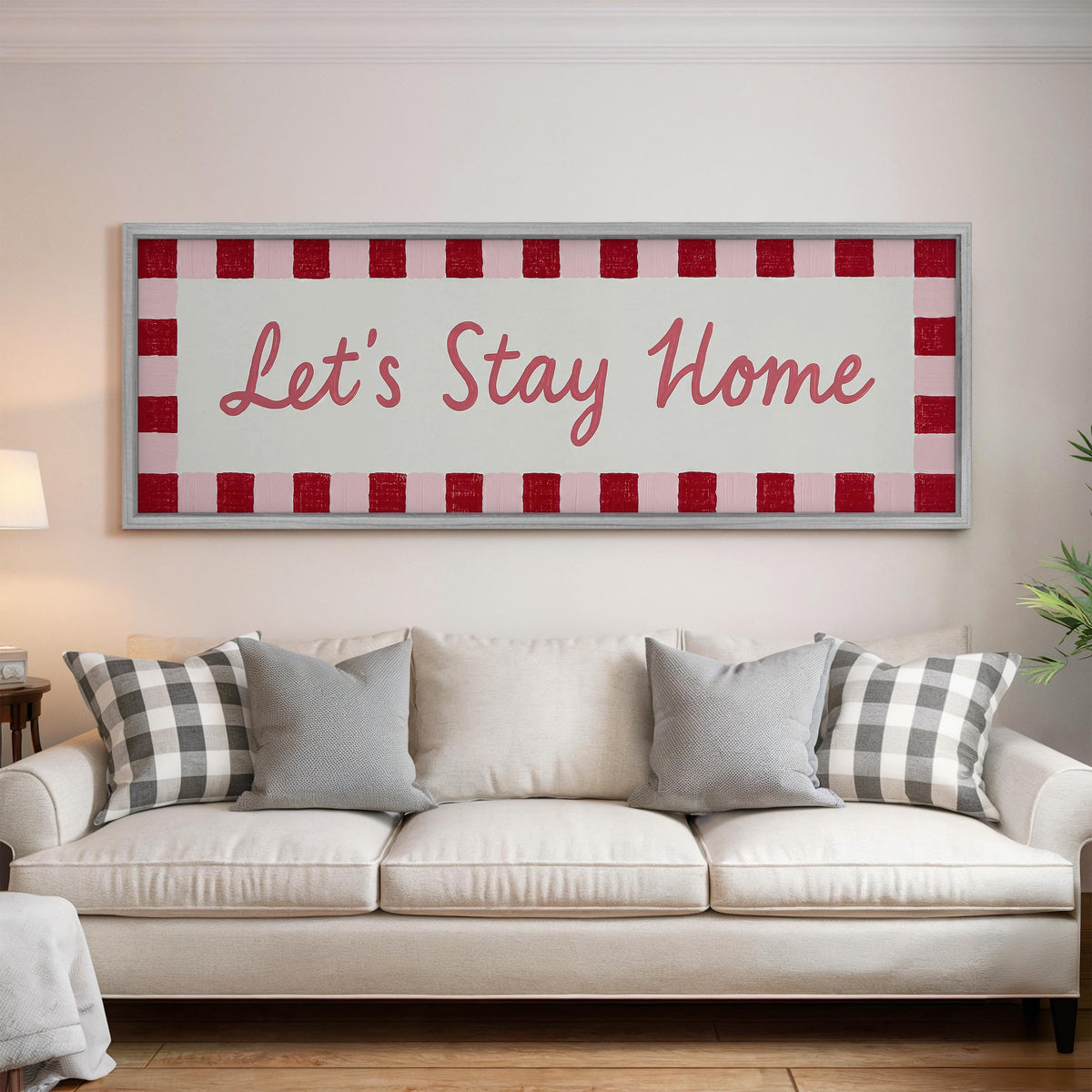 Let's stay home sign with a red checked border panoramic canvas print above a white sofa in a bright living room