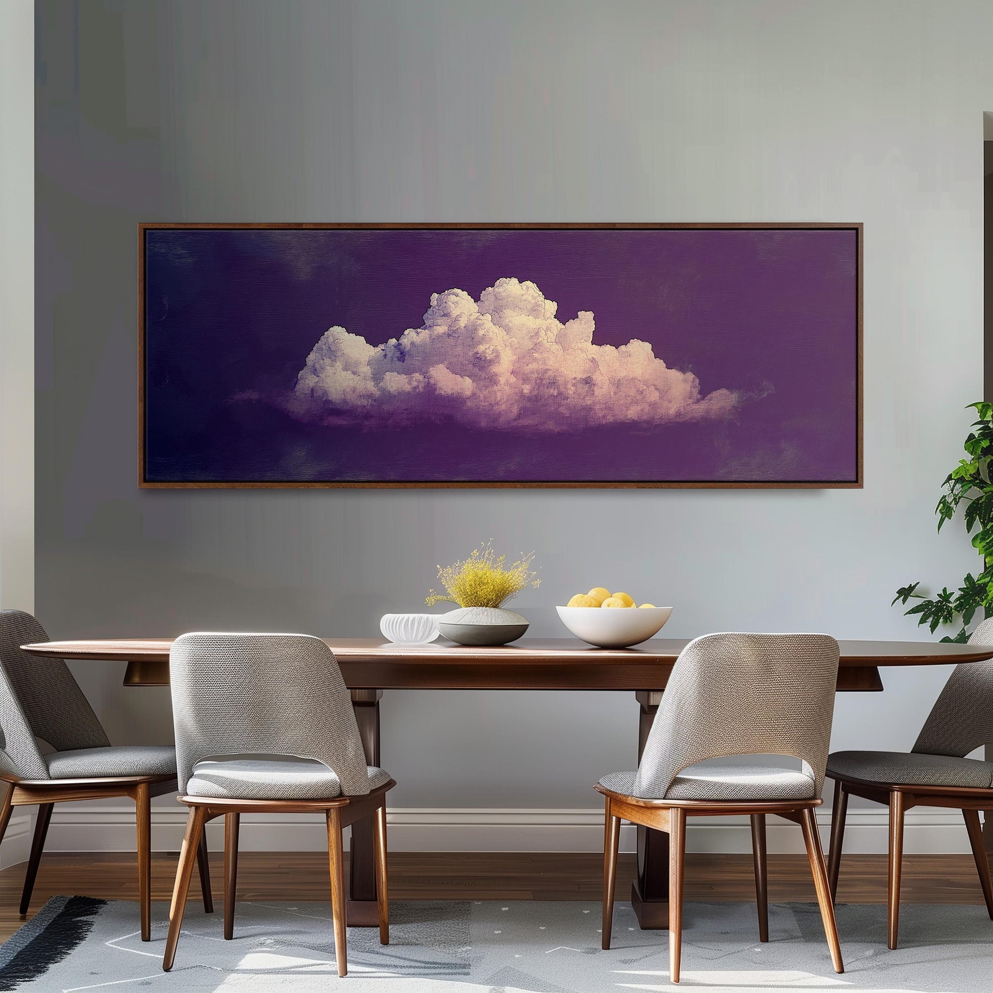 a dining room with a wooden table and four chairs. Above the table, there is a large framed picture of a cloud painted in purple and pink colors. The table is set with a bowl of fruit and a vase of flowers, creating a cozy and inviting atmosphere.