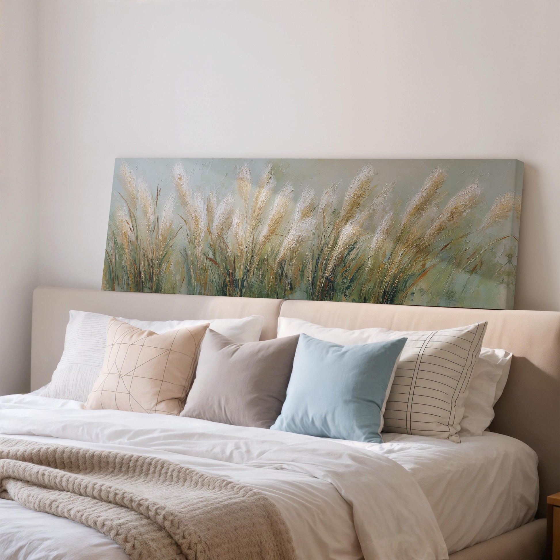 a cozy bedroom with a large bed adorned with white sheets and a blue pillow. Above the bed, there is a painting of tall grasses, adding a touch of nature to the room's decor.