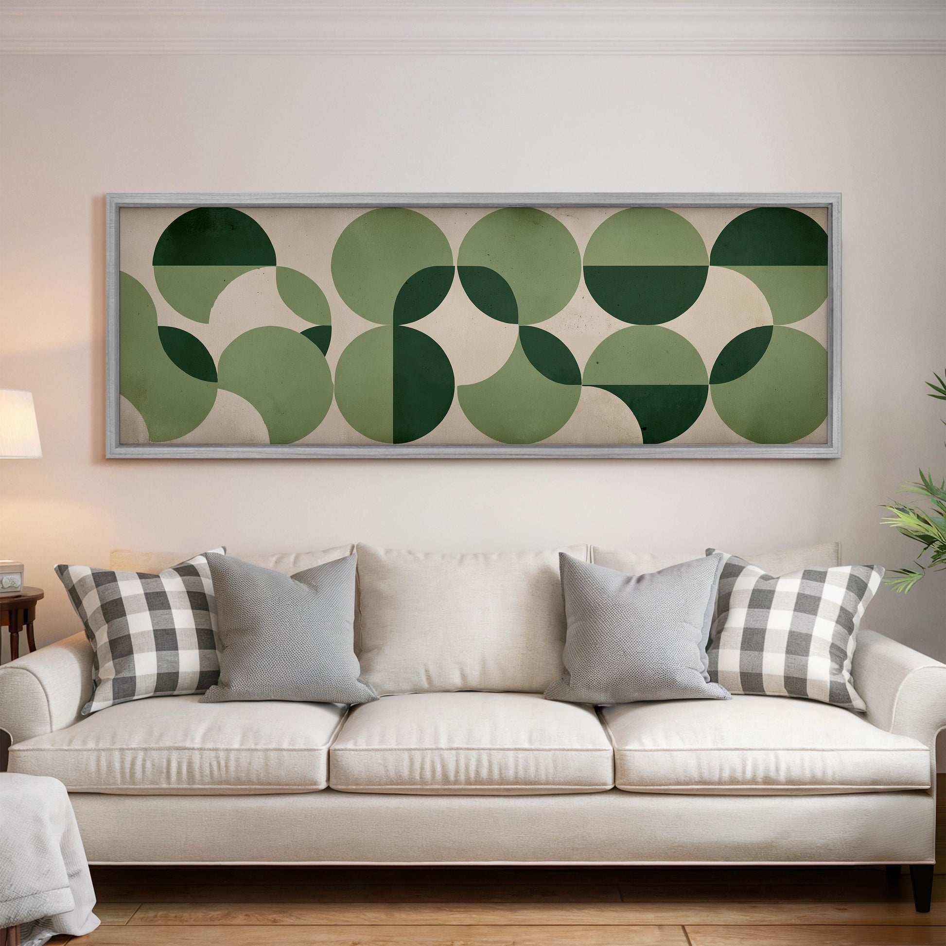 a living room with a white sofa adorned with gray and white plaid throw pillows. Above the sofa, there is a large framed artwork with a geometric design of green circles and lines.