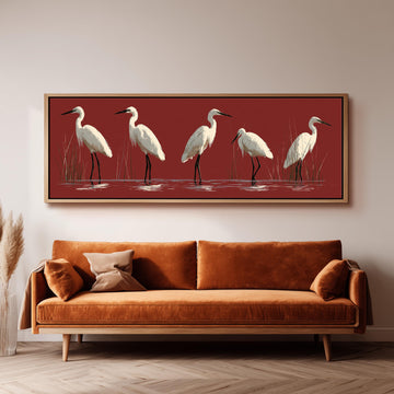 White egrets wading on crimson red long horizontal canvas print above a sofa in a living room