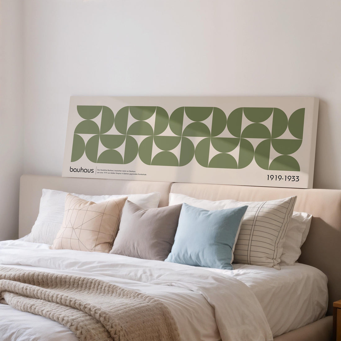 a large poster of a geometric pattern on a wall above a bed with white linens and various pillows.