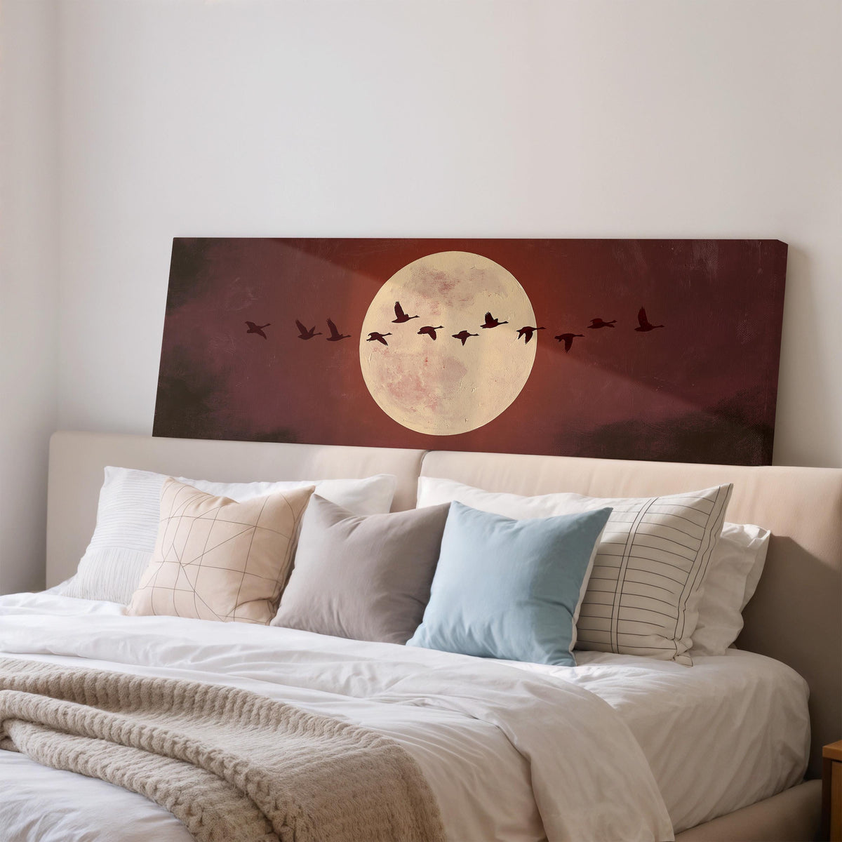Geese crossing a pale moon on maroon wide panoramic canvas print above a bed in a bedroom