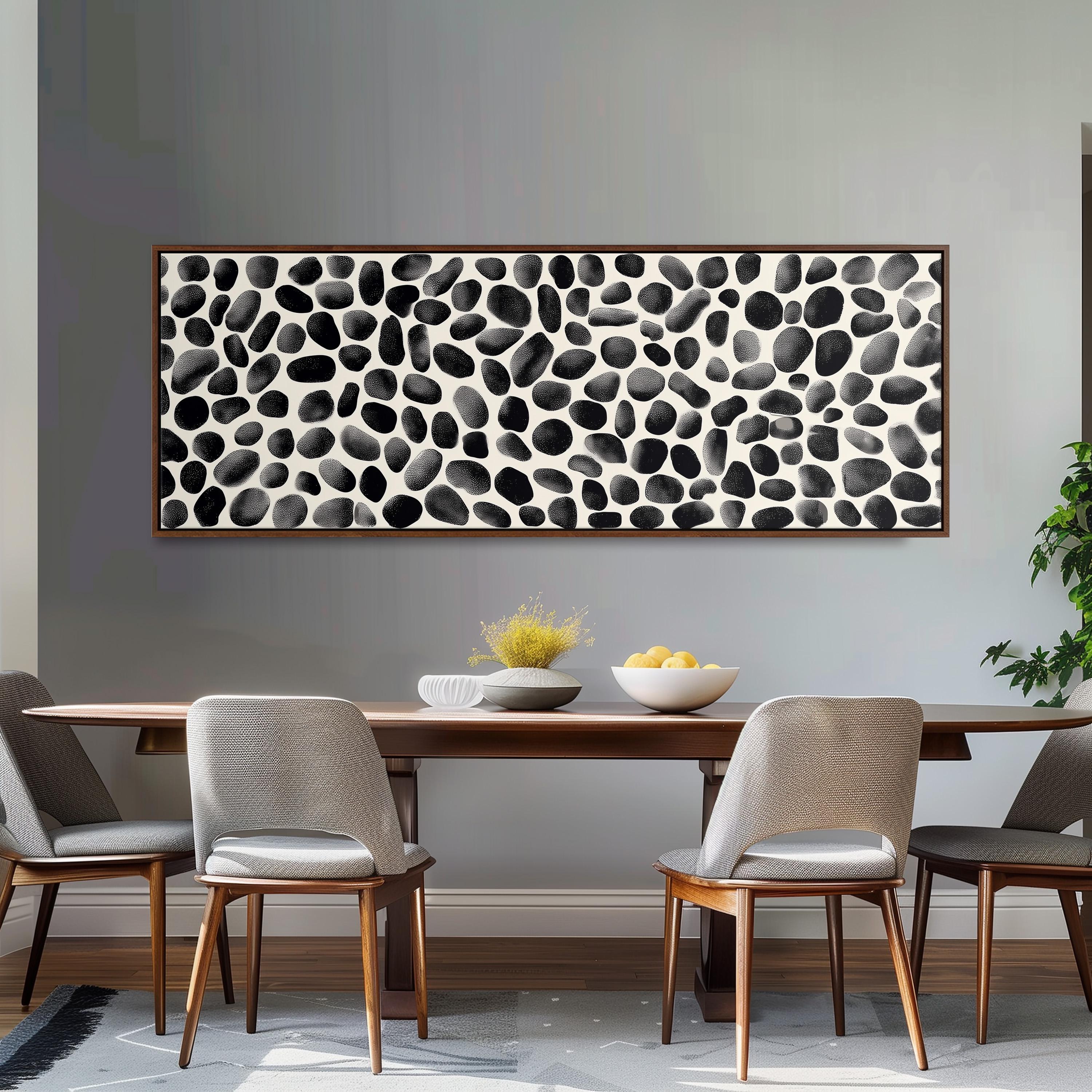 a dining room with a wooden table and four chairs. Above the table, there is a large black and white abstract painting with a repeating pattern of black and white circles. The table is set with a bowl of fruit and a vase of flowers, creating a cozy and inviting atmosphere.