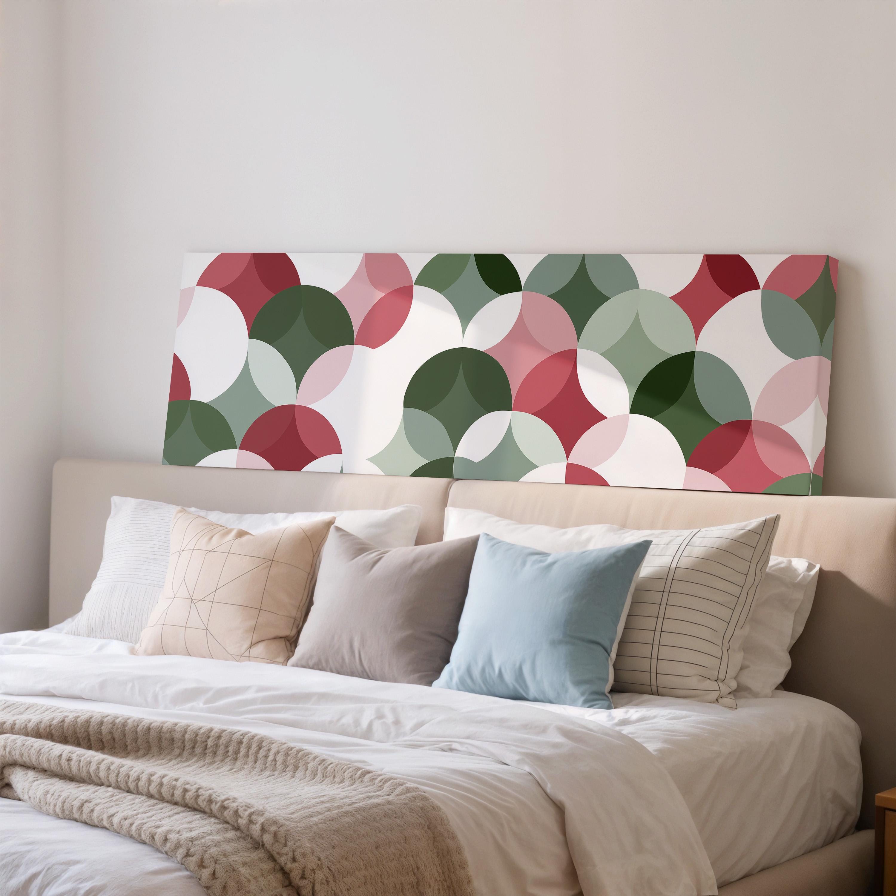 a cozy bedroom scene with a bed adorned with a variety of pillows and a blanket. The bed is positioned against a wall, with a large canvas print featuring a repeating pattern of circles in different colors hanging above it. The overall atmosphere of the room is warm and inviting, with the colorful circles on the canvas adding a touch of vibrancy to the space.