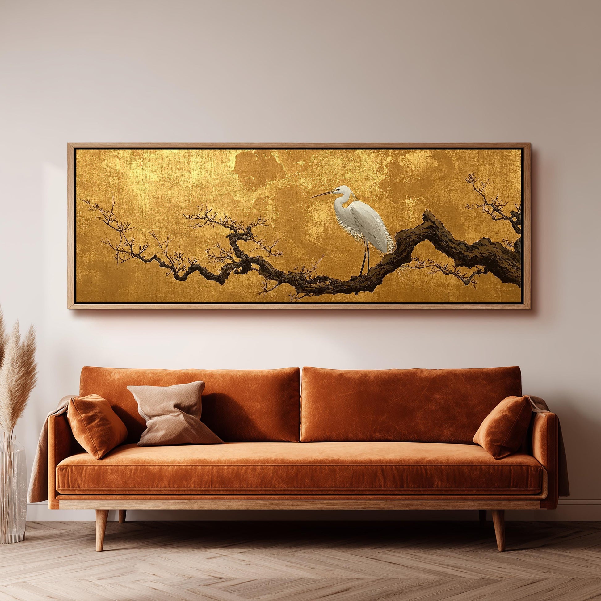 a large, ornate gold-framed painting of a white egret perched on a branch, hanging on a wall above a brown sofa.