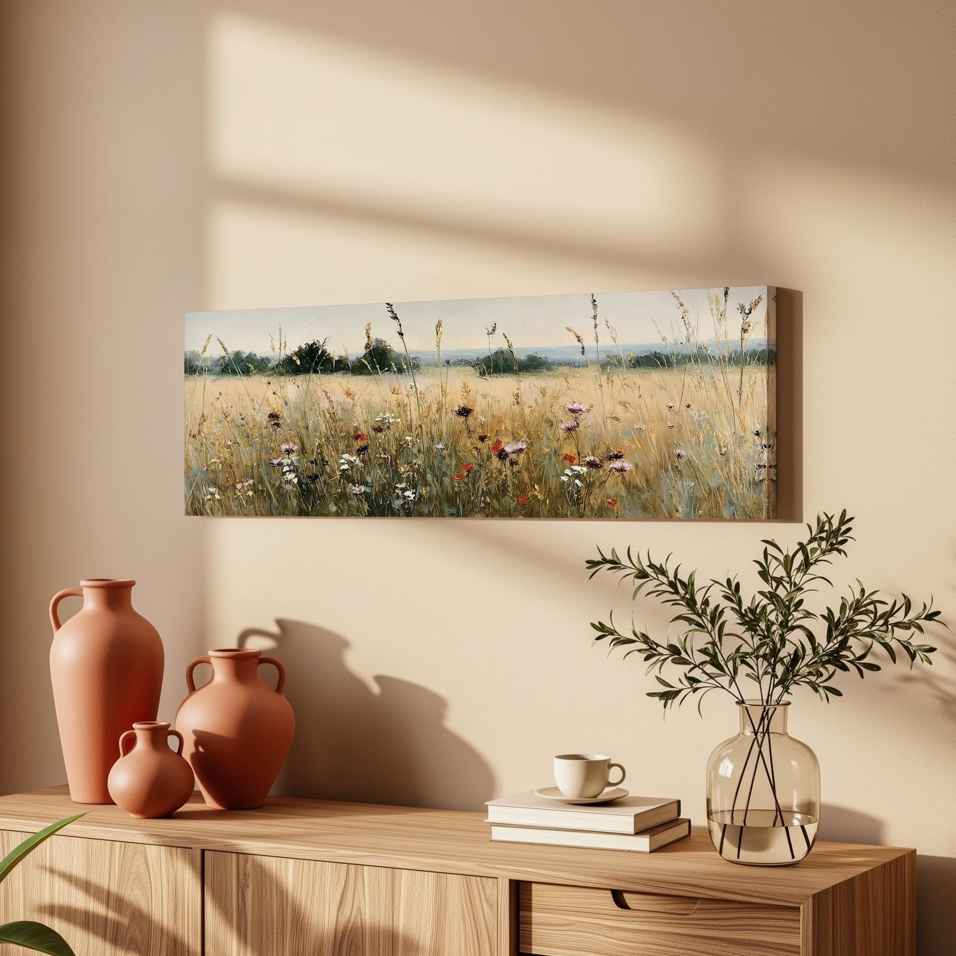 a wooden cabinet with a vase of greenery, a stack of books, and a painting of a field of flowers hanging on the wall above it.