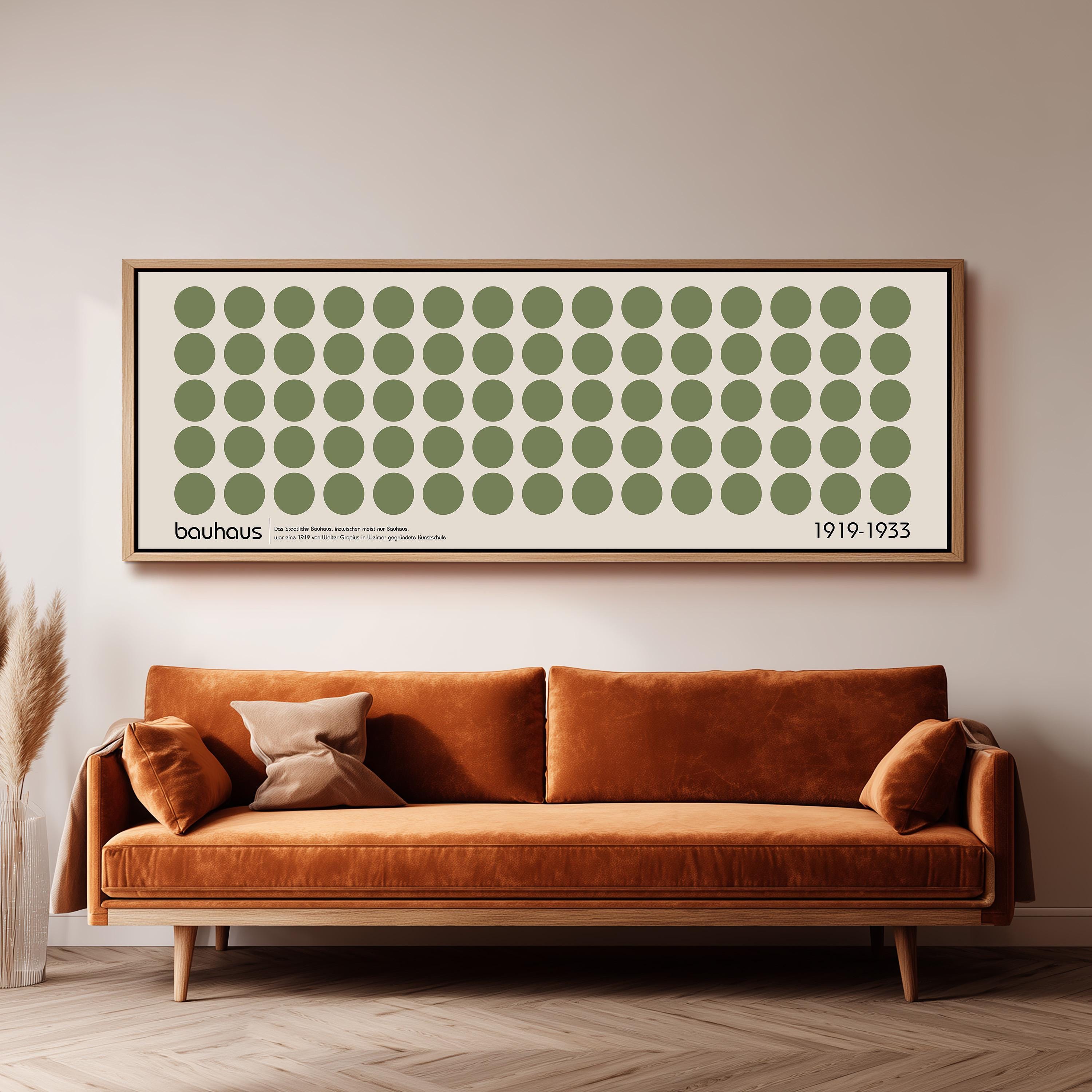 a large framed poster of a repeating pattern of green circles on a white background, hanging on a wall above a brown sofa.
