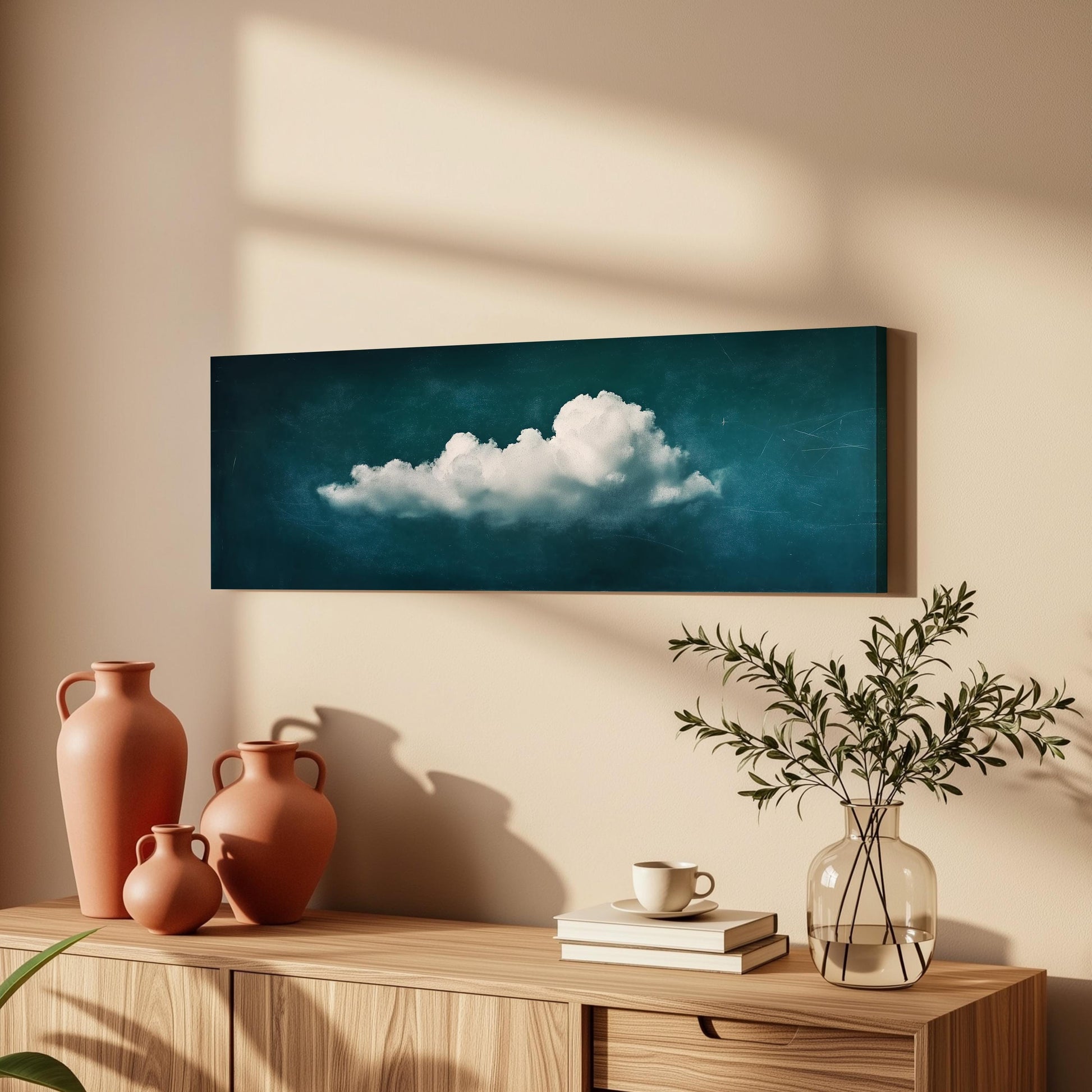 a wooden cabinet with a vase of greenery, a coffee cup, and a stack of books on top. Above the cabinet, there is a framed painting of a cloud on the wall.