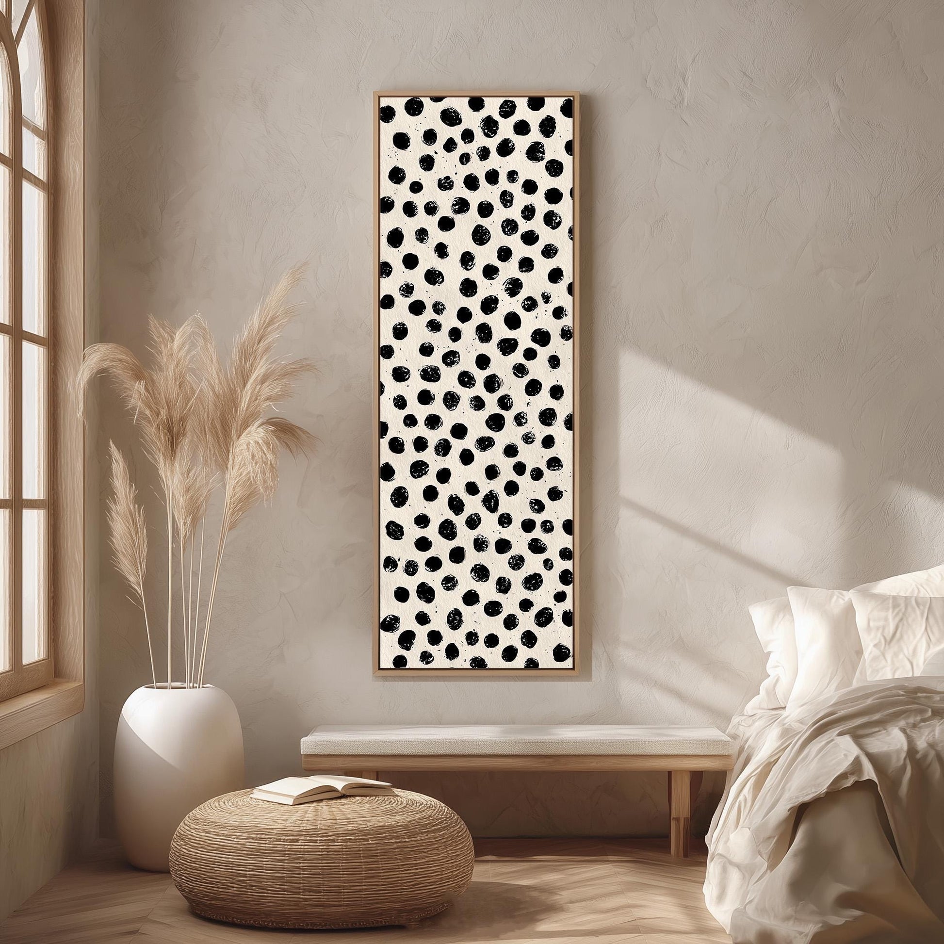 a minimalist bedroom interior with a large black and white polka dot print hanging on the wall, a white bed with a white pillow, a white ottoman, and a tall potted plant.