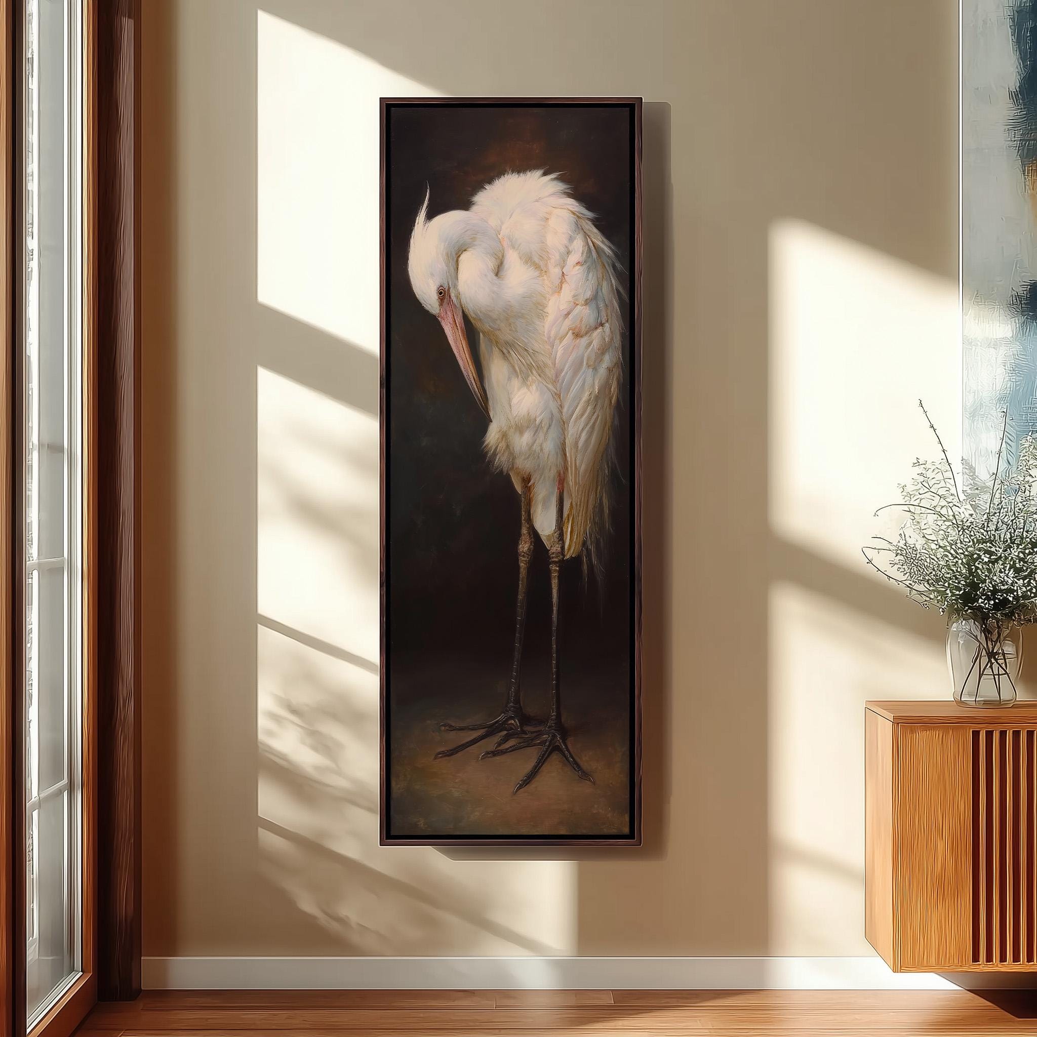 a large painting of a white heron standing on one leg against a dark background, hanging on a wall in a room with a wooden cabinet and a vase of flowers.