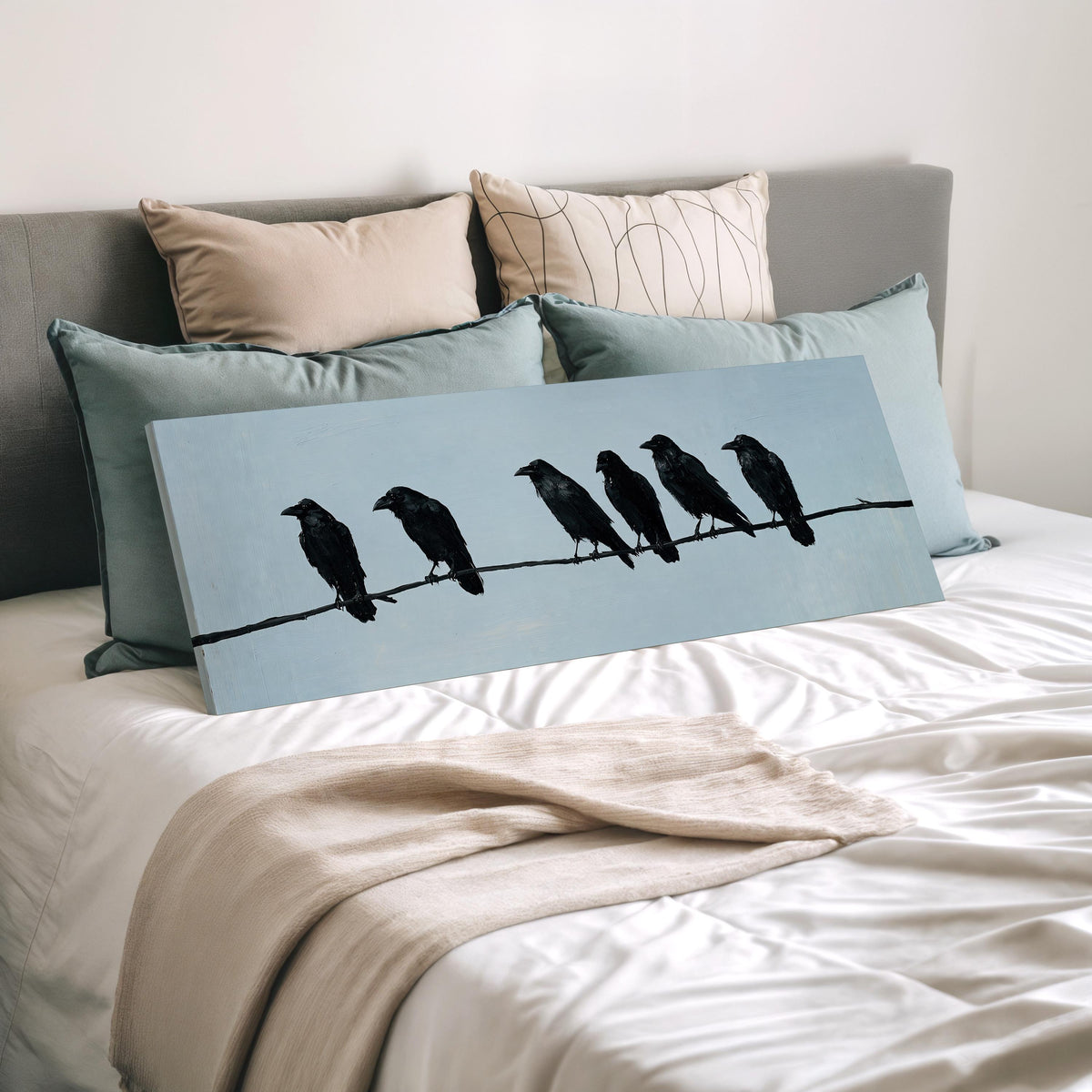 Ravens spaced along a wire wide panoramic canvas print laid on a bed to show its size