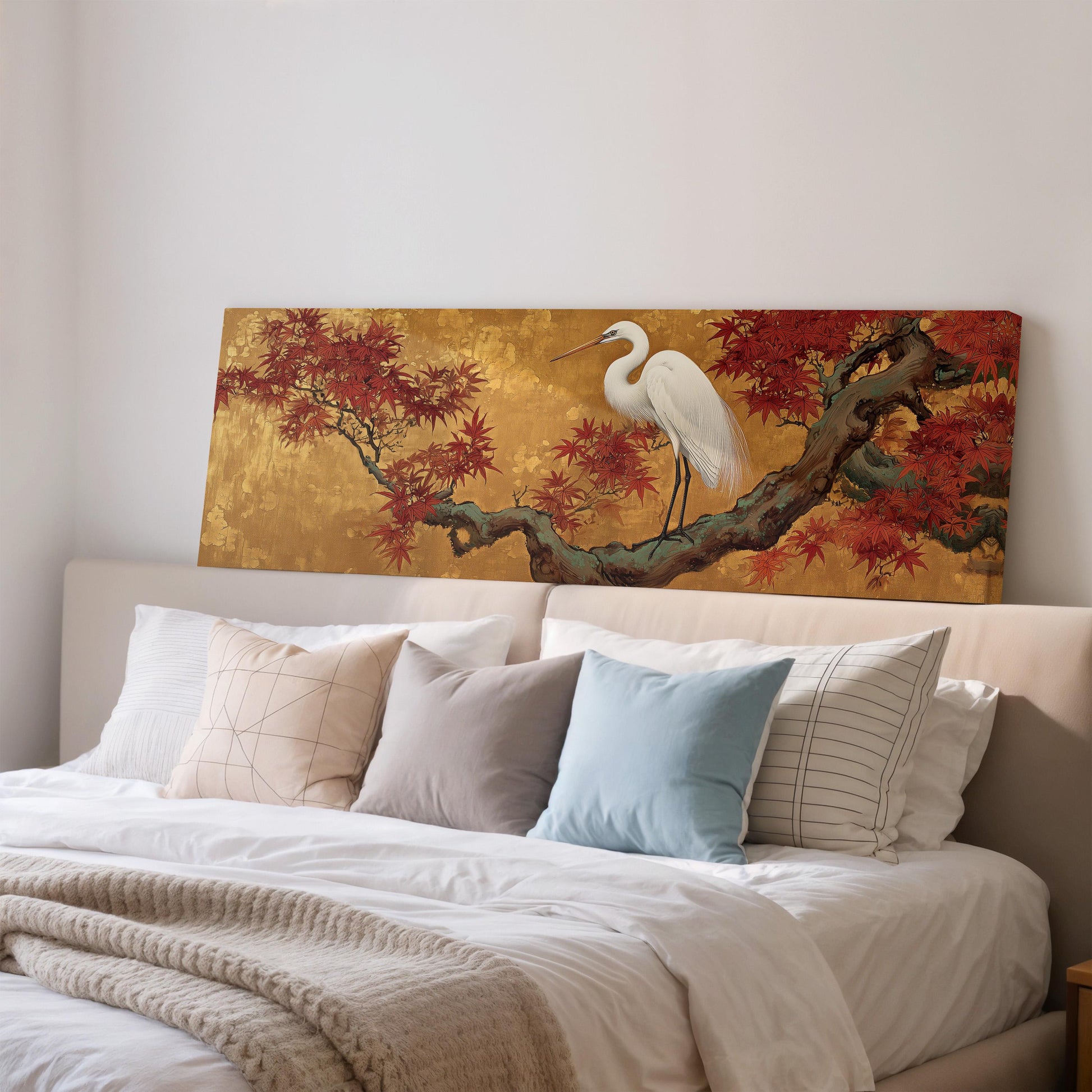 a large painting of a white crane perched on a branch with red leaves, displayed on a wall above a bed with white pillows and a gray blanket.