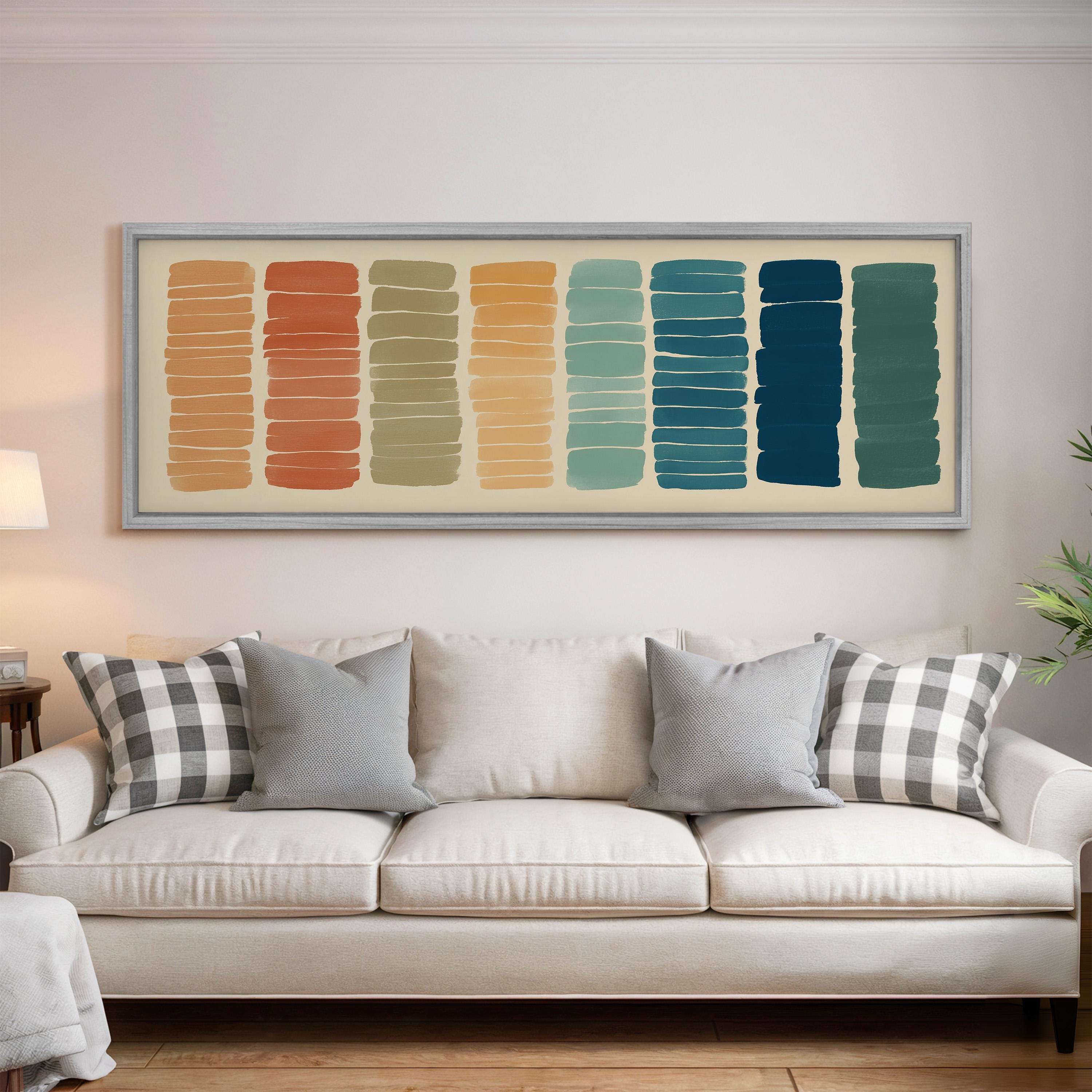 a white couch with gray and black plaid throw pillows, and a framed abstract art piece with vertical stripes in various colors is hanging above it on the wall.