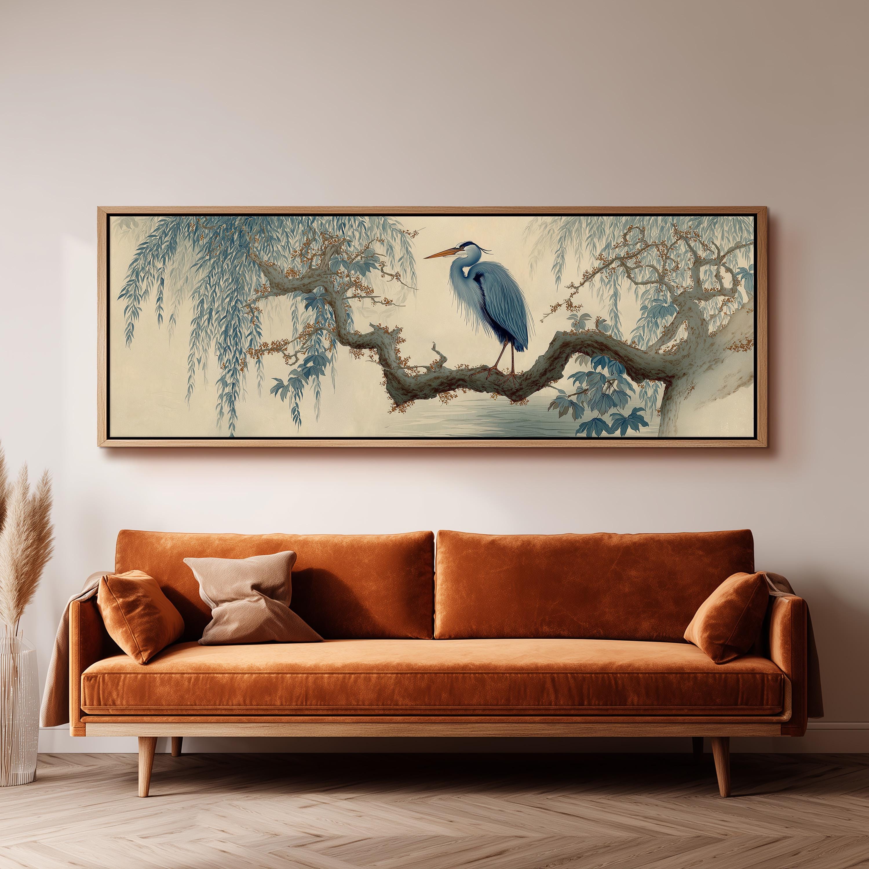 a large, framed painting of a blue heron perched on a branch, hanging on a wall above a brown sofa.