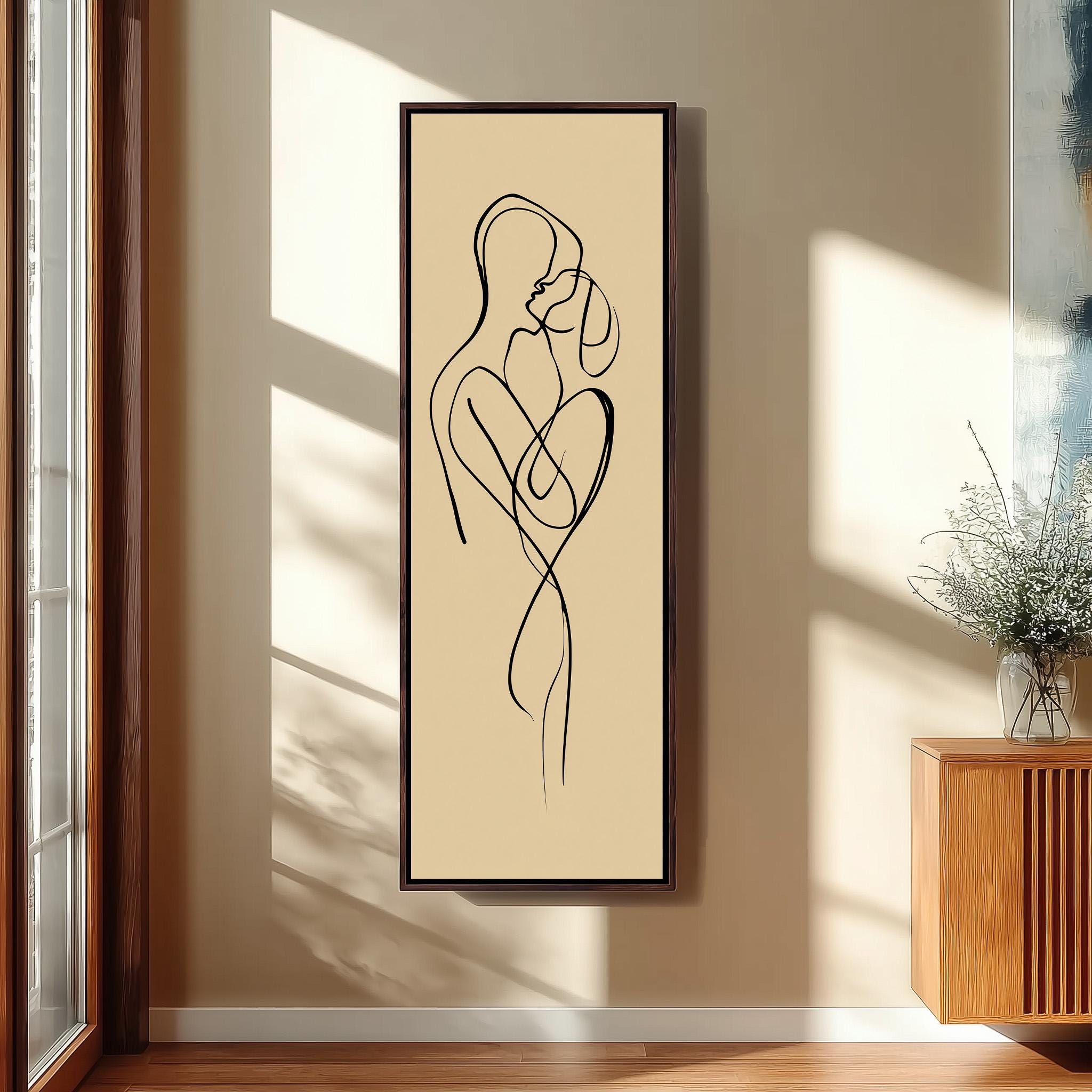 a framed abstract art piece depicting a couple embracing, hanging on a wall in a room with a wooden cabinet and a vase of flowers.