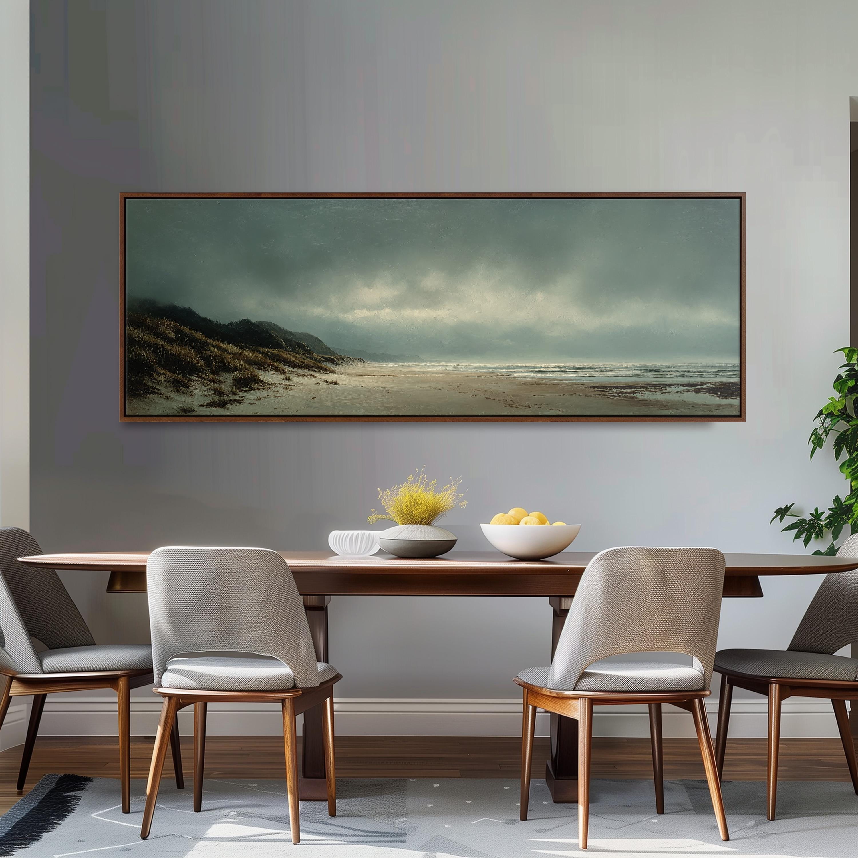 a dining room with a large painting of a beach scene hanging on the wall above a wooden dining table with four chairs. The painting depicts a cloudy sky over a sandy beach, with a few trees visible in the background.