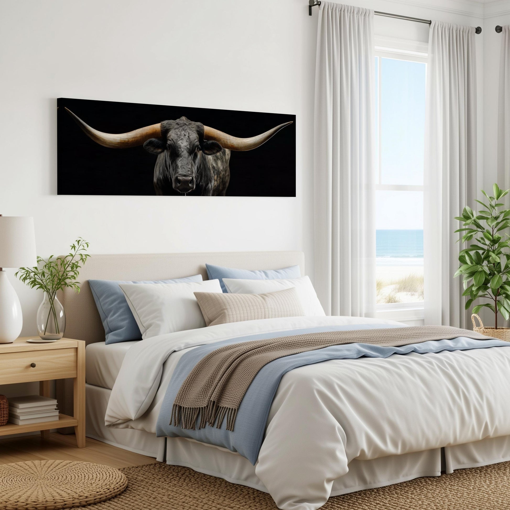 a bedroom with a large bed, a nightstand, and a window overlooking the ocean. The bed has a white comforter and a gray throw blanket. There is a large black bull's head artwork hanging on the wall above the bed.