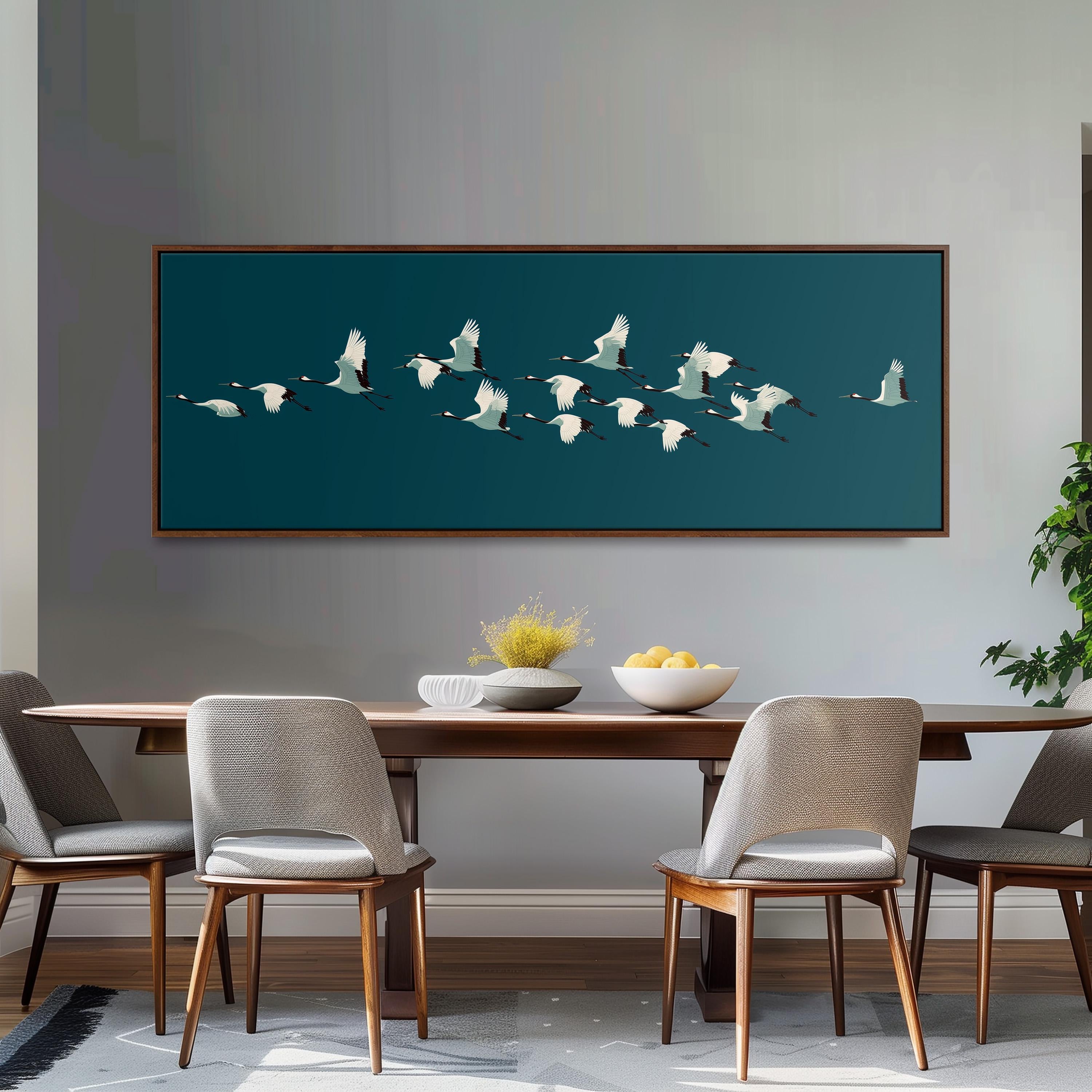 a dining room with a wooden table and four chairs, a large framed artwork of a flock of white birds in flight above the table, and a bowl of fruit on the table.