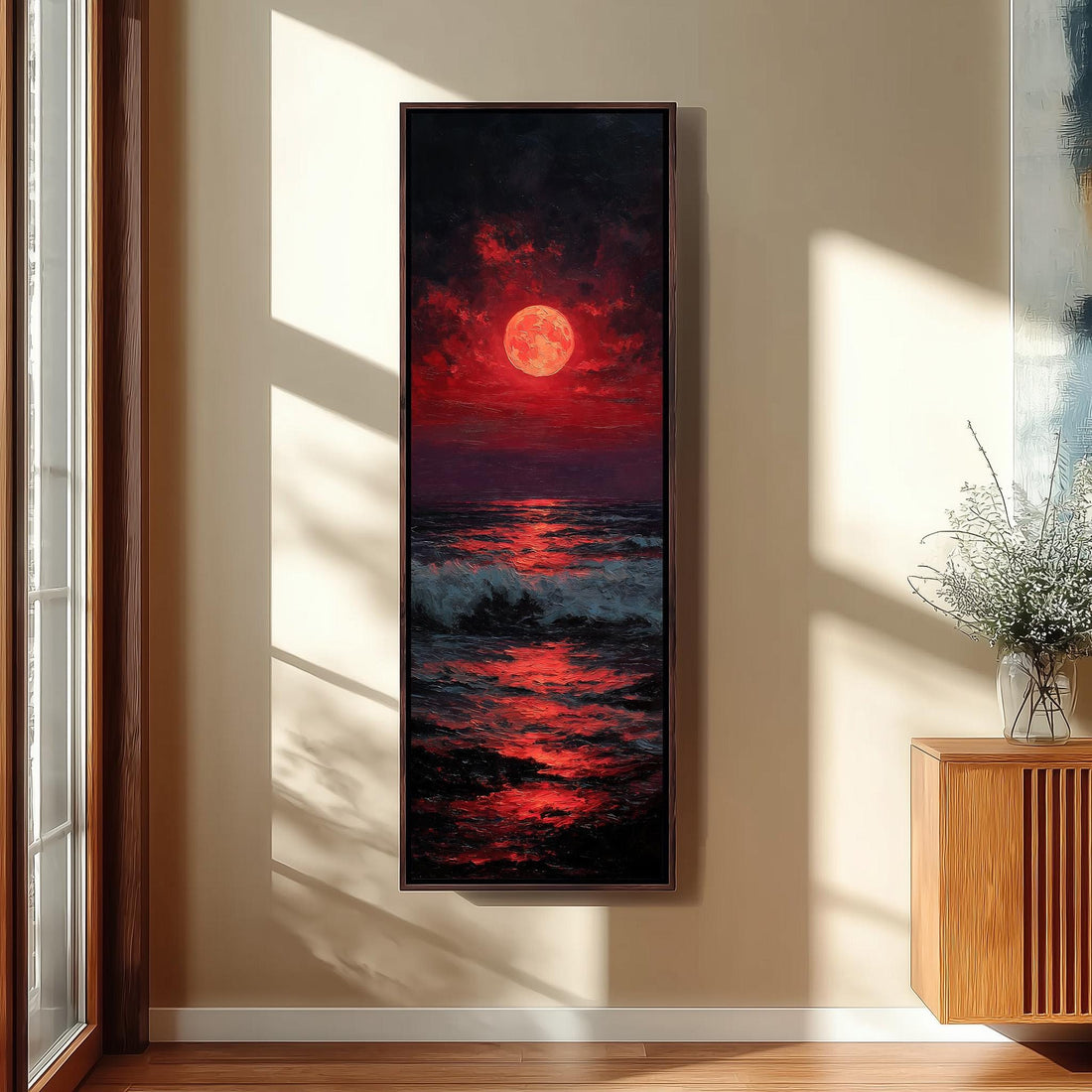 a large, framed painting of a sunset over the ocean, with a large, red moon in the sky. The painting is hanging on a wall in a hallway, with a staircase visible in the background.