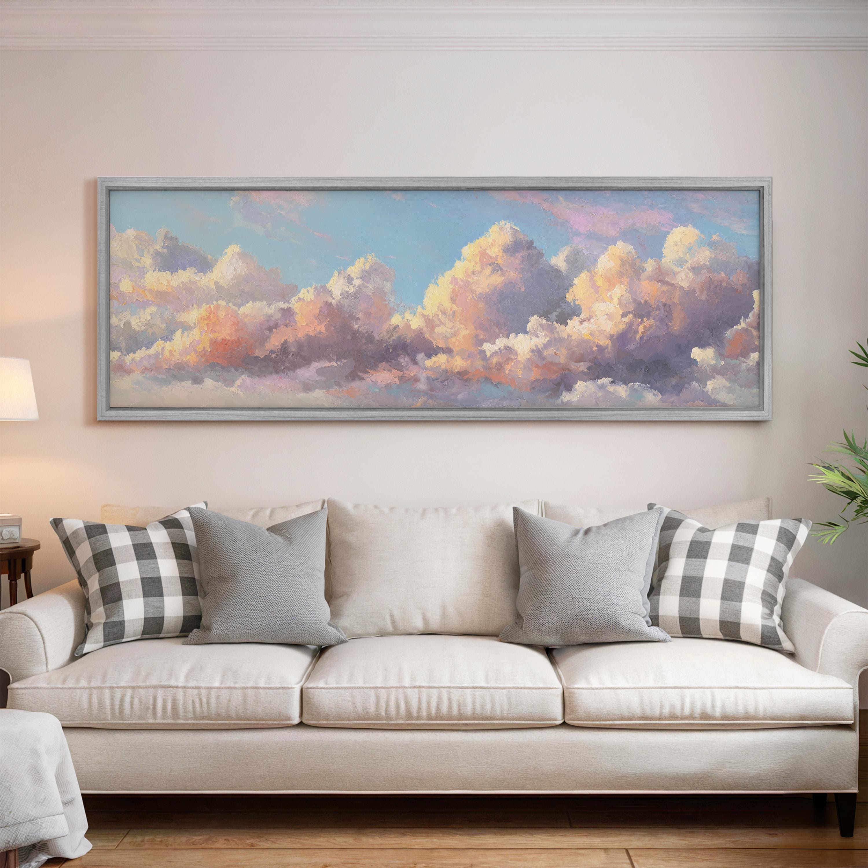 a large, framed painting of a cloudy sky hanging on a wall above a white couch with gray and black plaid throw pillows.