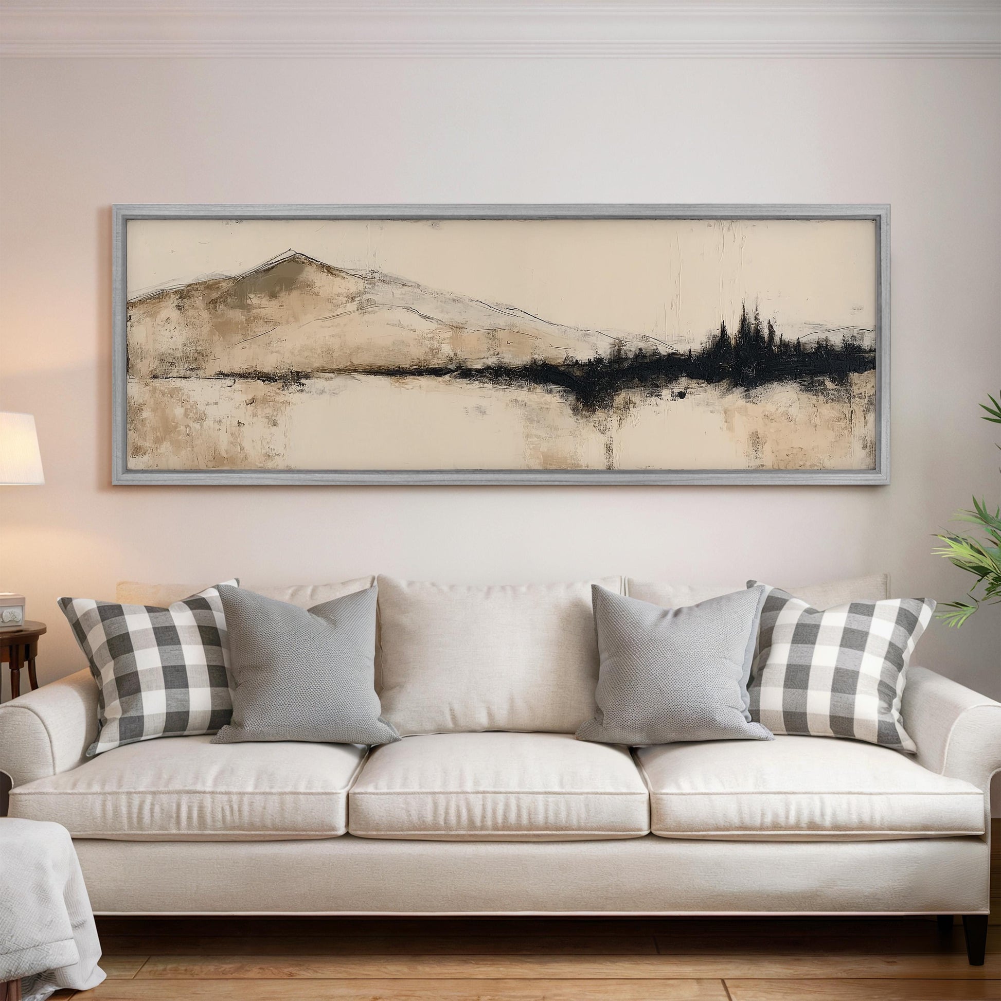 a living room with a white sofa adorned with gray and white plaid throw pillows. Above the sofa, there is a large framed artwork depicting a mountain landscape.