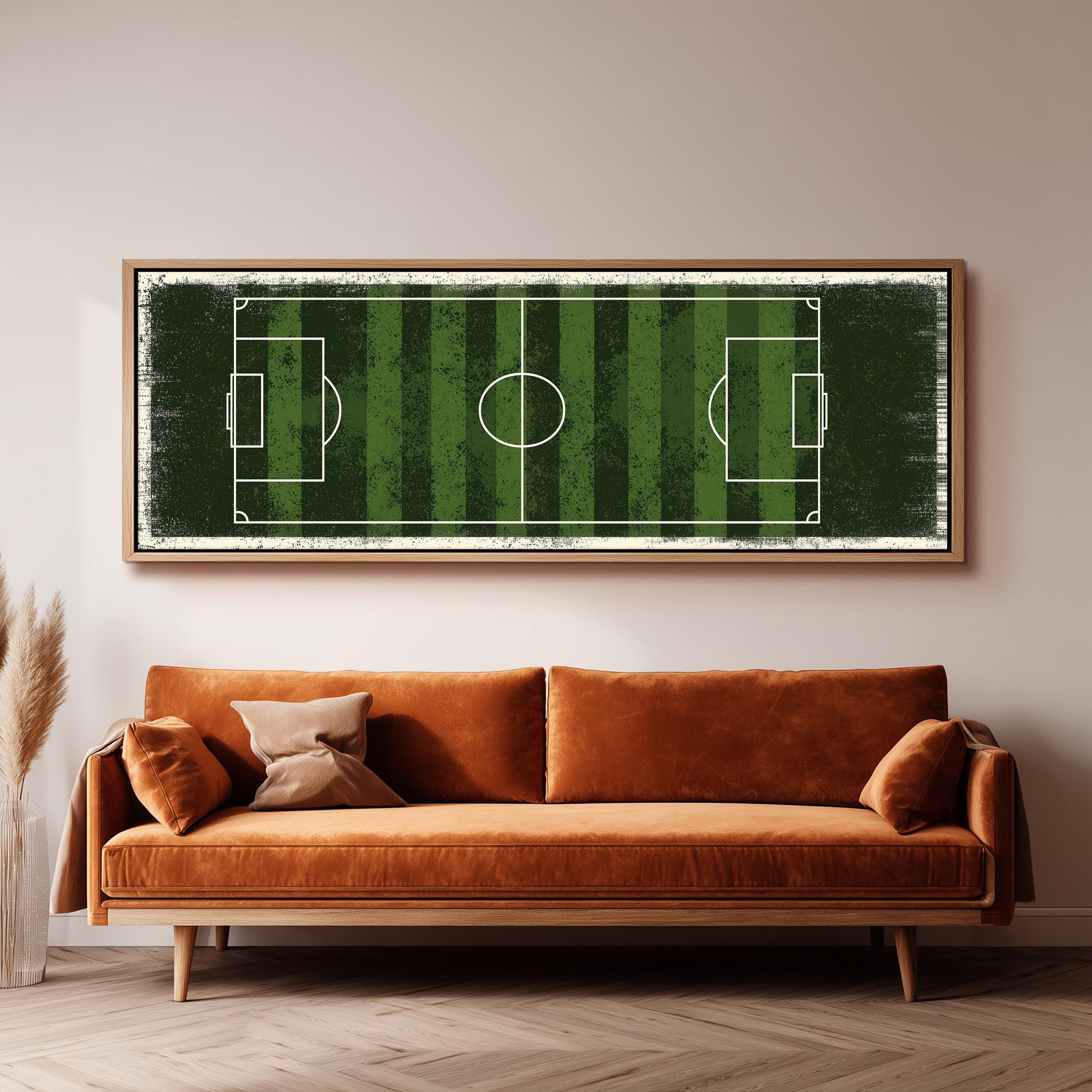 a large, framed picture of a soccer field hanging on a wall above a brown sofa.