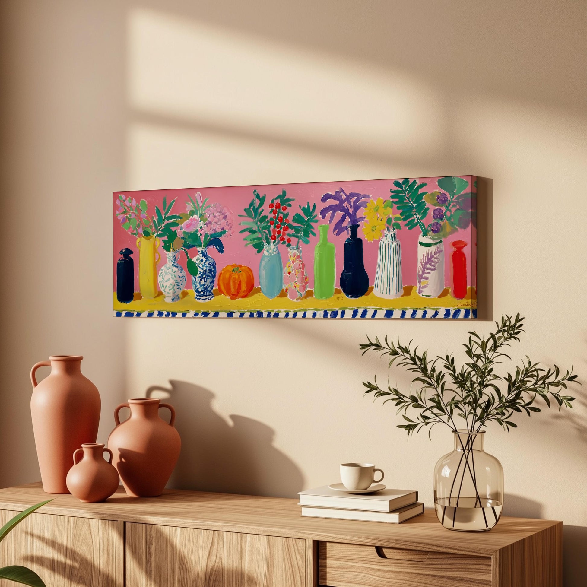 a vibrant painting of colorful vases and flowers displayed on a wall above a wooden cabinet. The cabinet has a few decorative items, including a coffee cup and a stack of books.