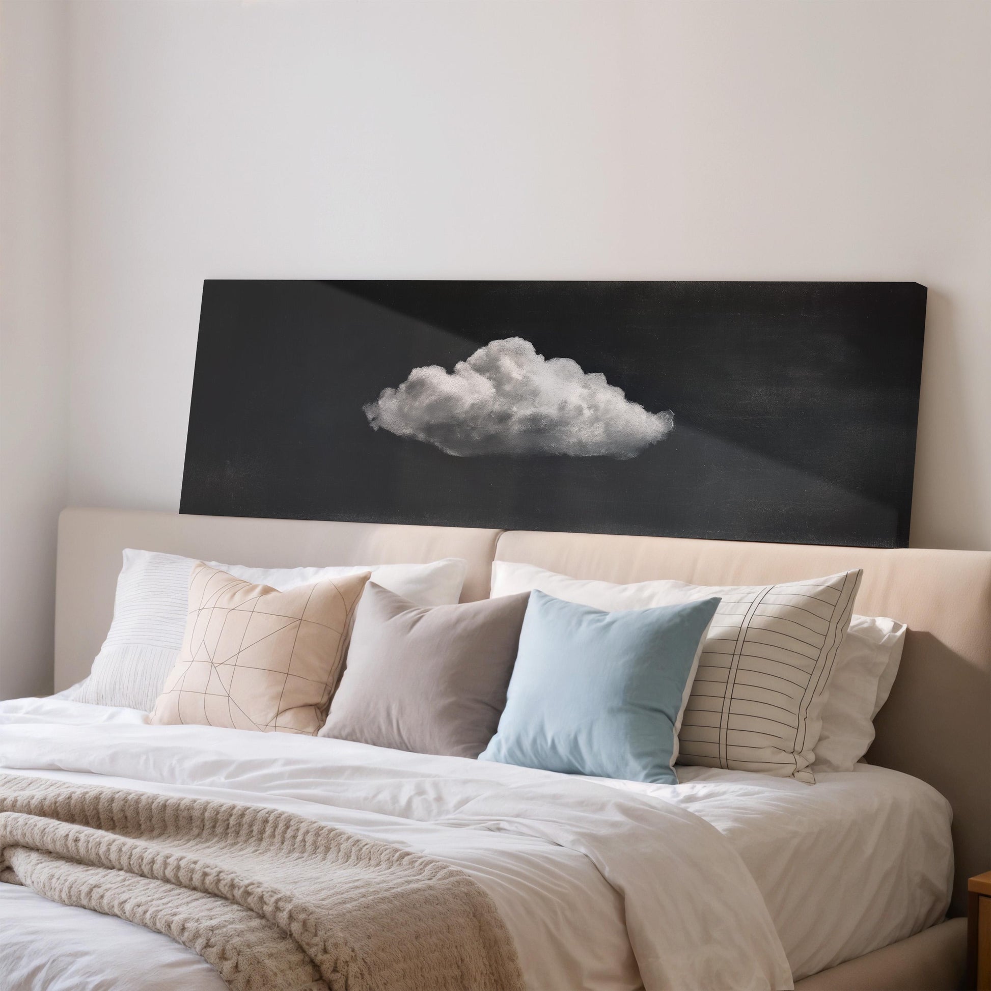 a cozy bedroom with a bed adorned with white sheets and a blue pillow. Above the bed, there is a black canvas with a white cloud design on it.