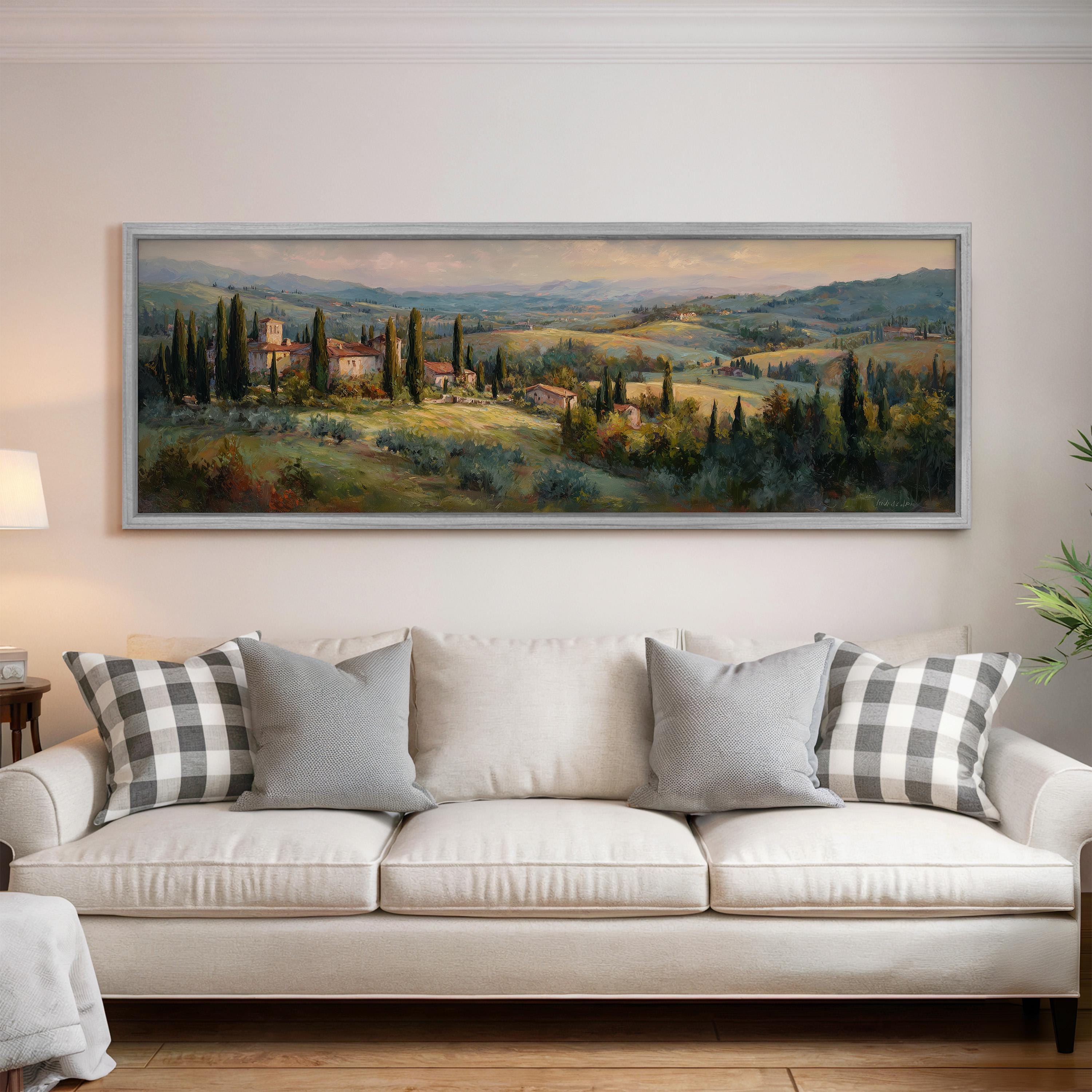 a large painting of a countryside landscape hanging on a wall above a white sofa with gray and white patterned pillows.