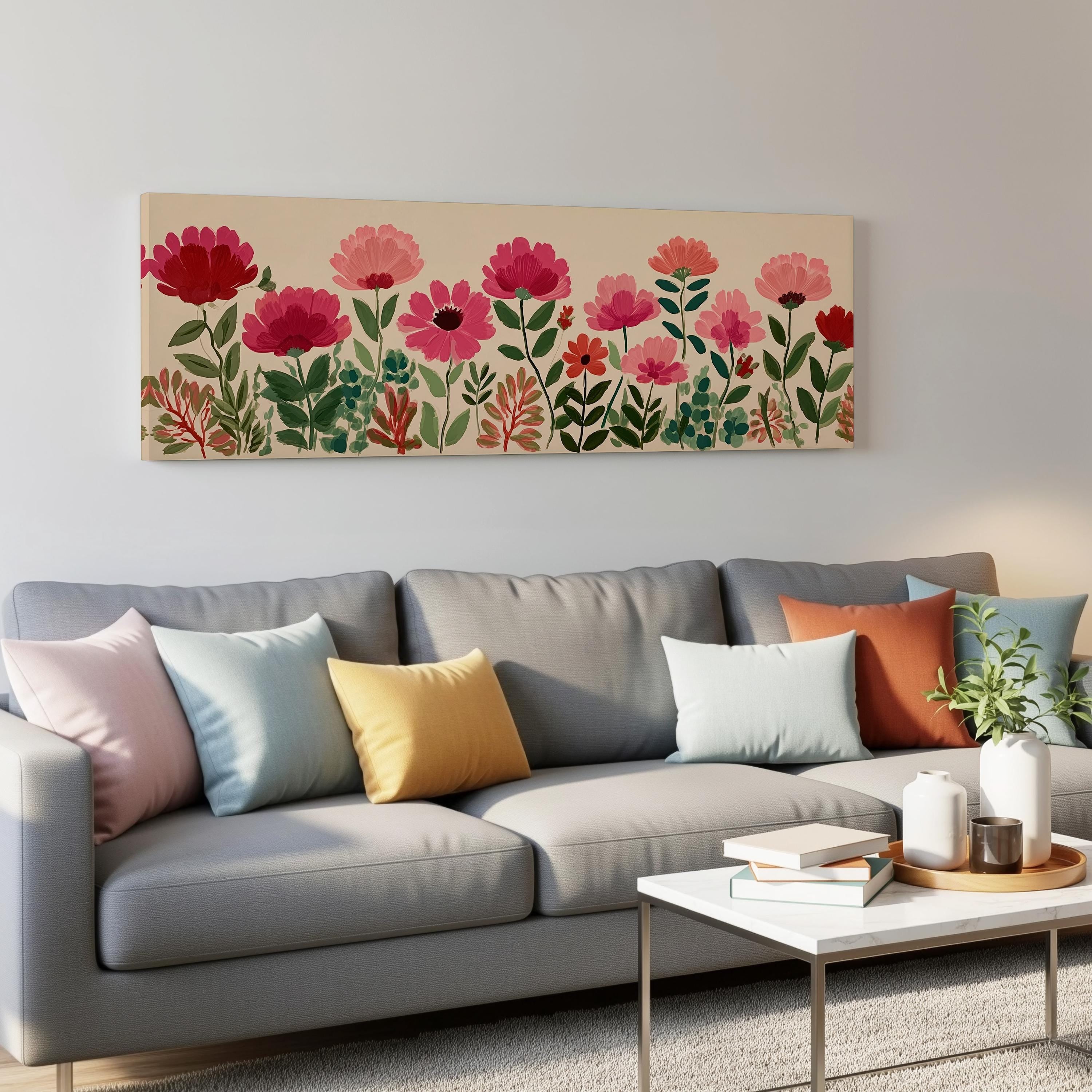 a cozy living room with a gray sofa adorned with colorful throw pillows. Above the sofa, there is a large canvas print depicting a vibrant floral arrangement of pink and red flowers. The room also includes a coffee table with books and a plant, creating a comfortable and inviting atmosphere.