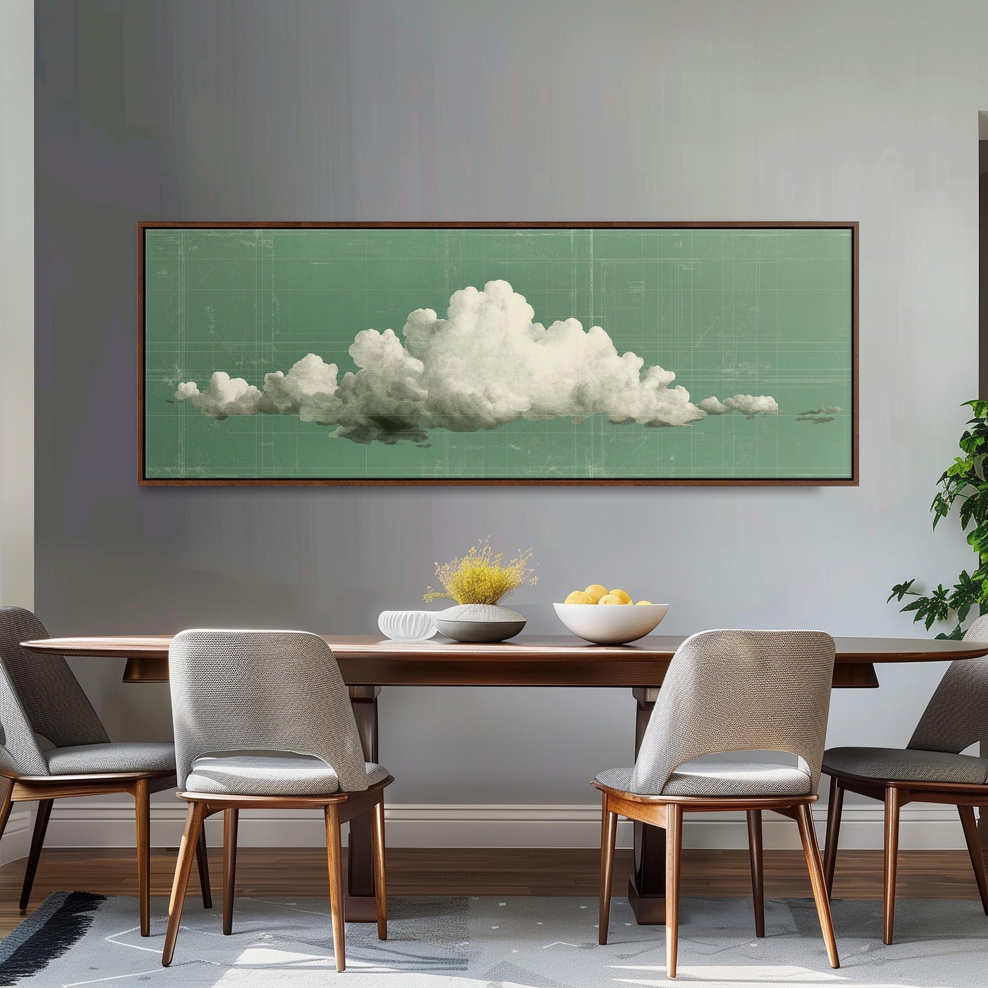 a dining room with a wooden table and four chairs. Above the table, there is a large framed picture of a cloud hanging on the wall. The table is set with a bowl of fruit and a vase of flowers, creating a cozy and inviting atmosphere.