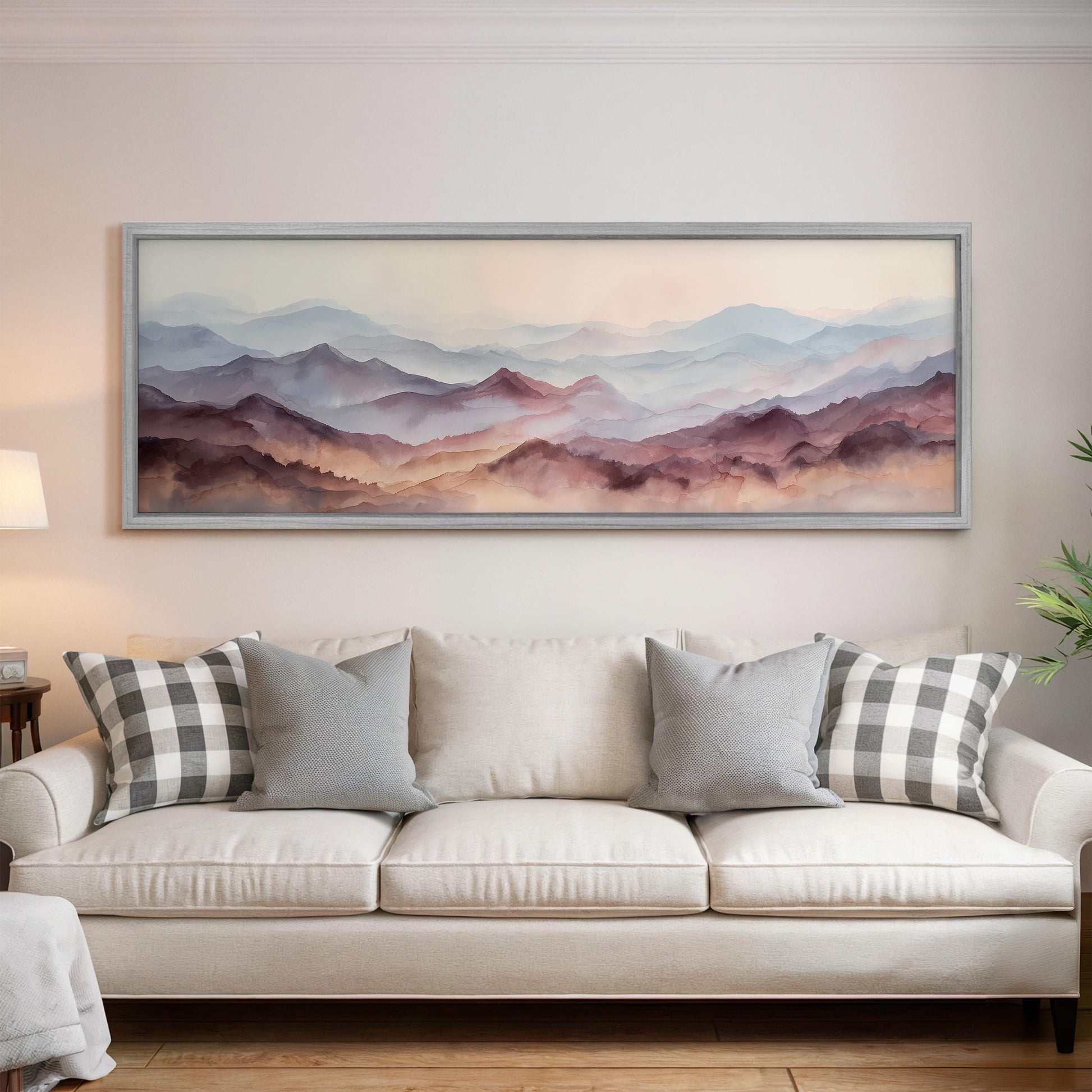 a large, framed painting of a mountain landscape hanging on a wall above a white sofa with gray and white patterned pillows.