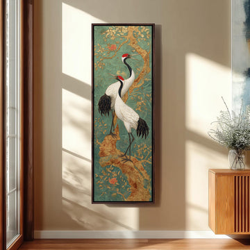 a large framed painting of two white birds with black and red accents, standing on a branch with green and gold accents, hanging on a wall in a room with a wooden cabinet and a vase of flowers.