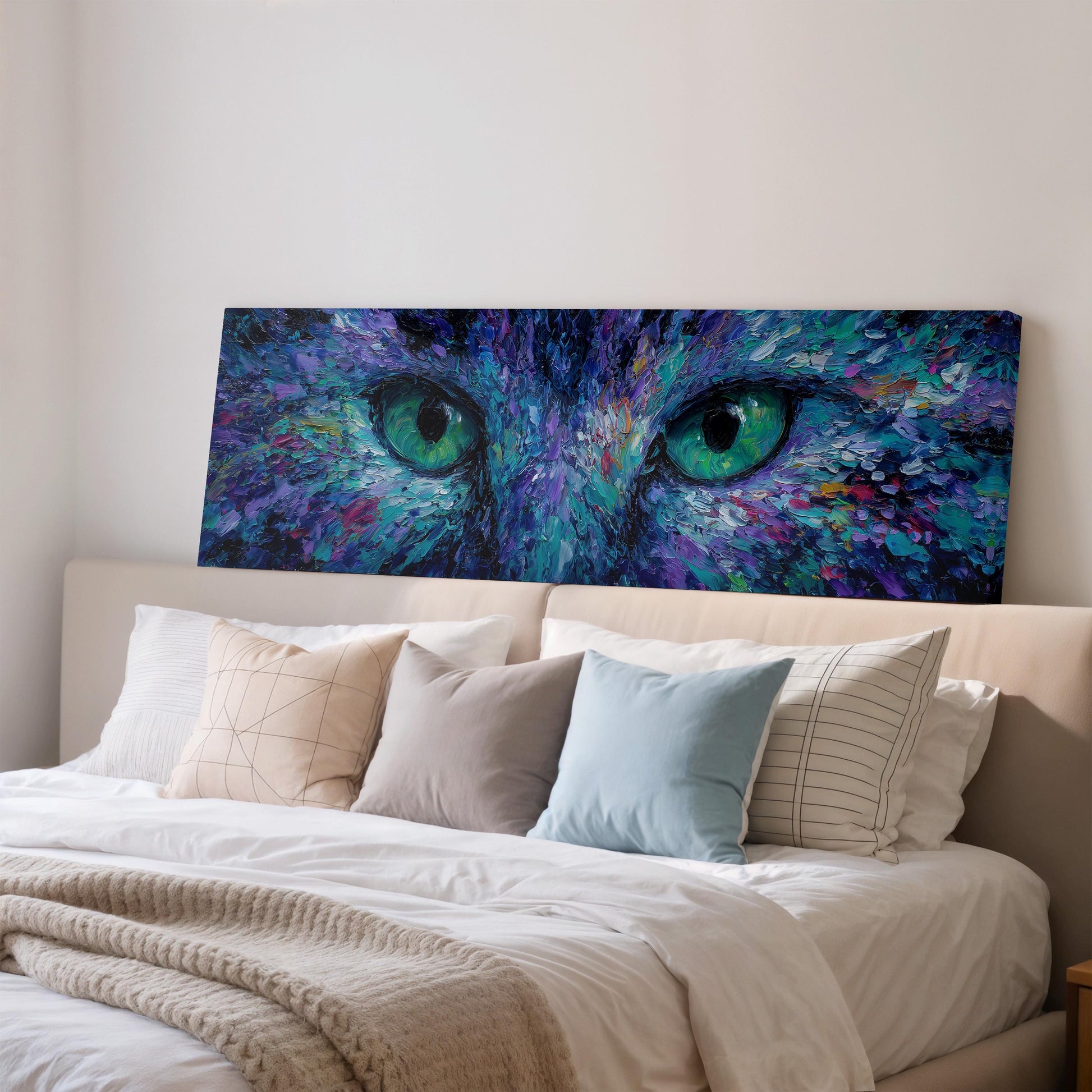 a large, colorful painting of a cat's face with striking green eyes, displayed on a wall above a bed with white bedding and pillows.