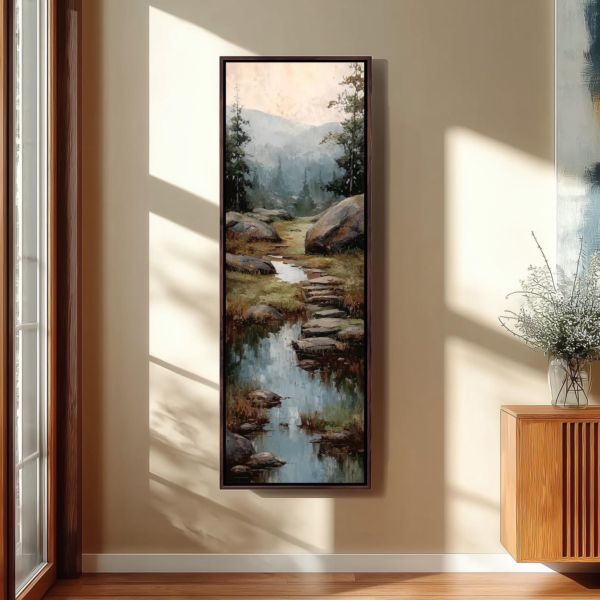 a large painting of a serene landscape with a stream, rocks, and trees hanging on a wall in a room with a wooden floor and a window.