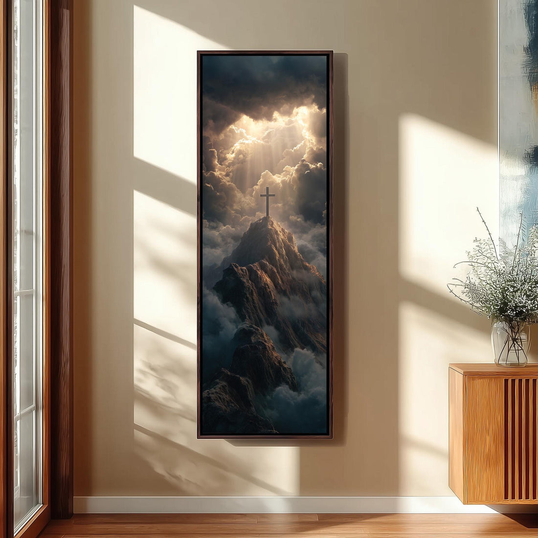 a large framed painting hanging on a wall, depicting a cross on a mountain peak surrounded by clouds and sunlight.