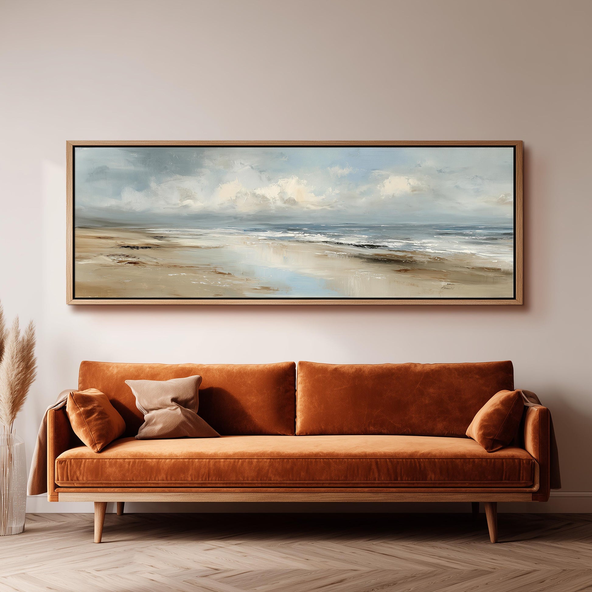 a large, rectangular painting of a beach scene hanging on a wall above a brown sofa with orange cushions.