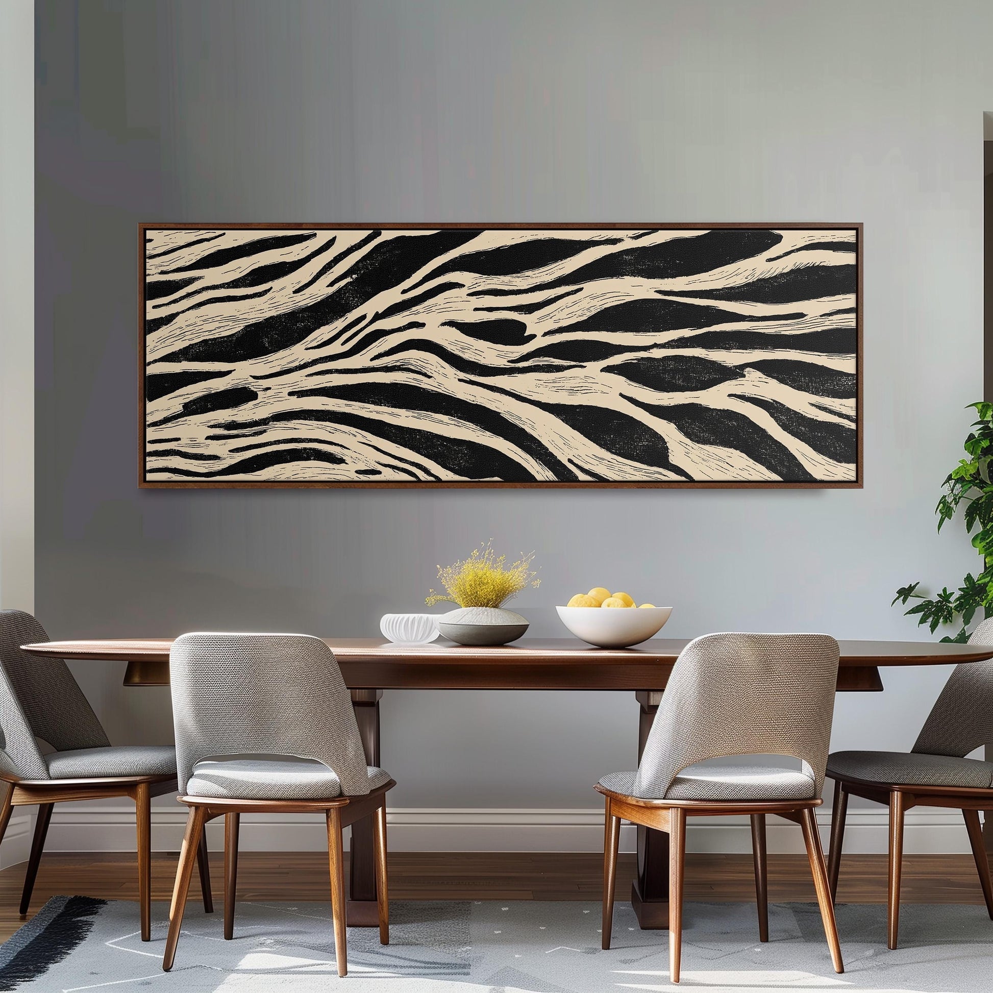 a dining room with a wooden table and four chairs. Above the table, there is a large black and white abstract painting hanging on the wall. On the table, there is a bowl of fruit and a vase of flowers.