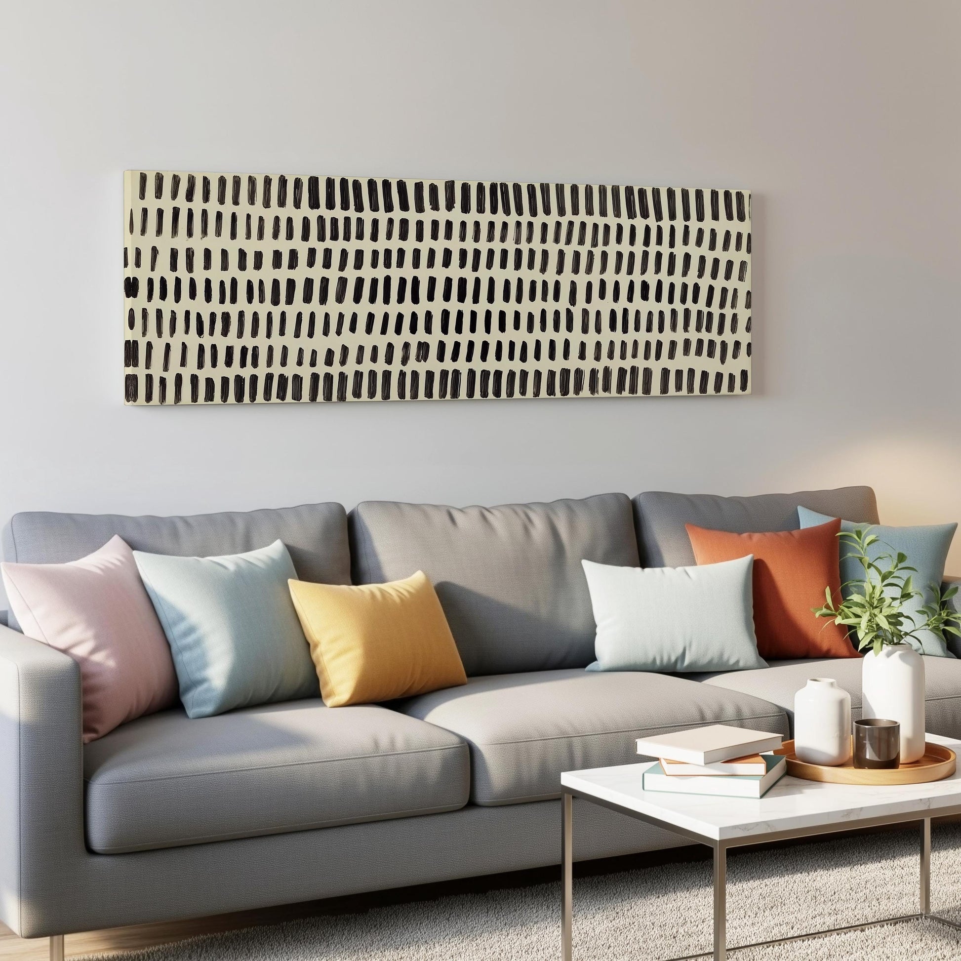 a modern living room with a gray sofa adorned with colorful throw pillows. Above the sofa, there is a large abstract painting with a black and white striped pattern. In front of the sofa, there is a white coffee table with a stack of books and a small plant.