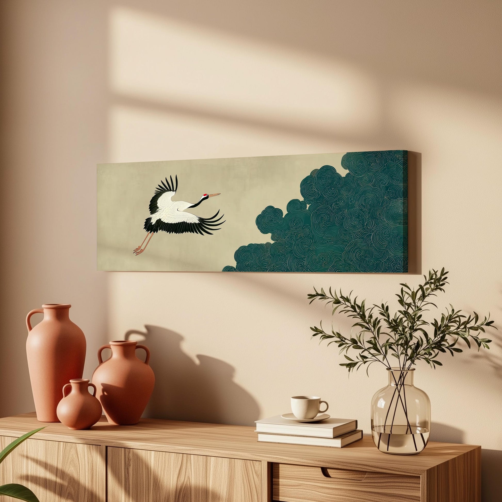 a wooden cabinet with a vase, a coffee cup, and a stack of books on top. Above the cabinet, there is a framed artwork depicting a crane in flight.