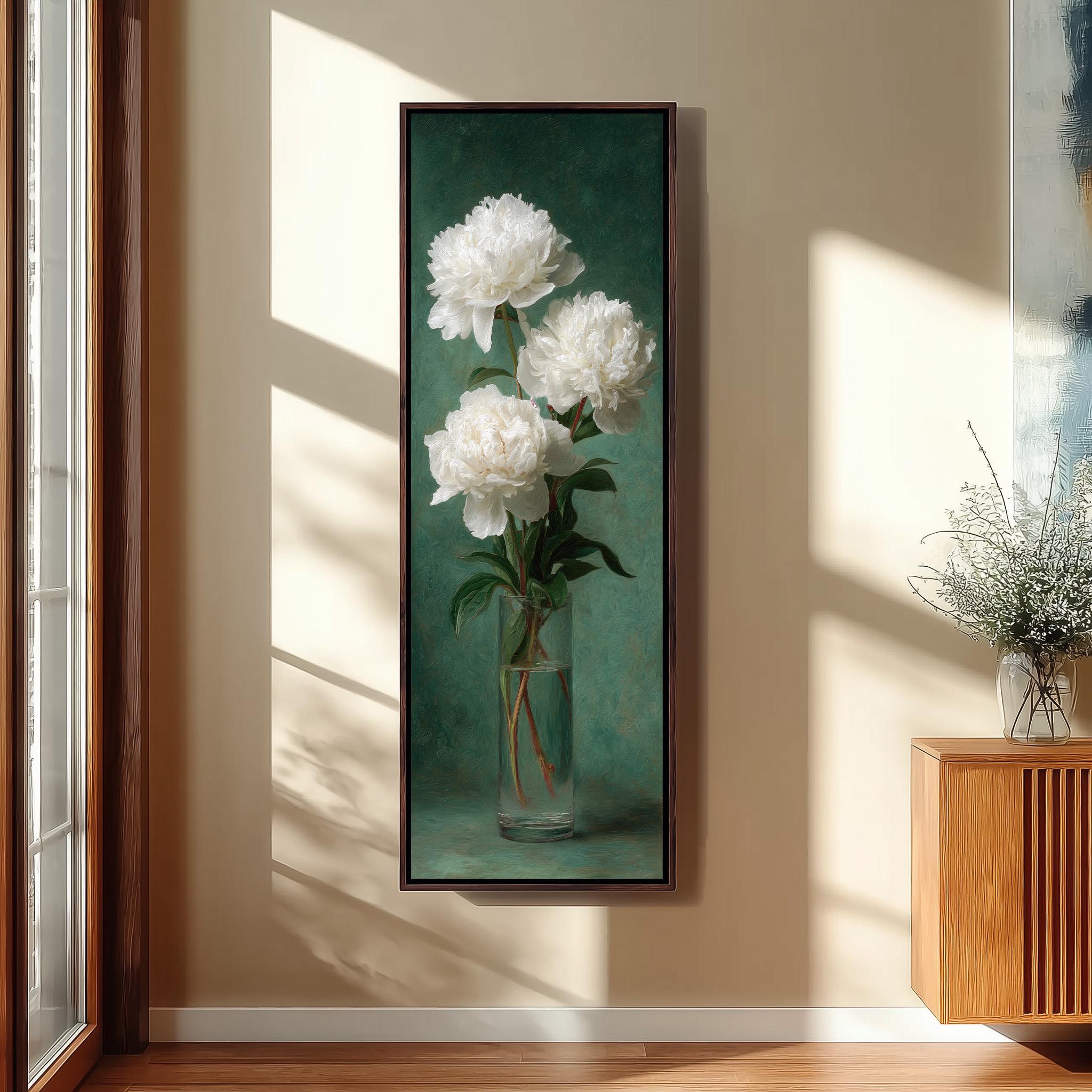 A framed painting of three white peonies in a clear vase is hanging on a wall in a room with a wooden cabinet and a window.