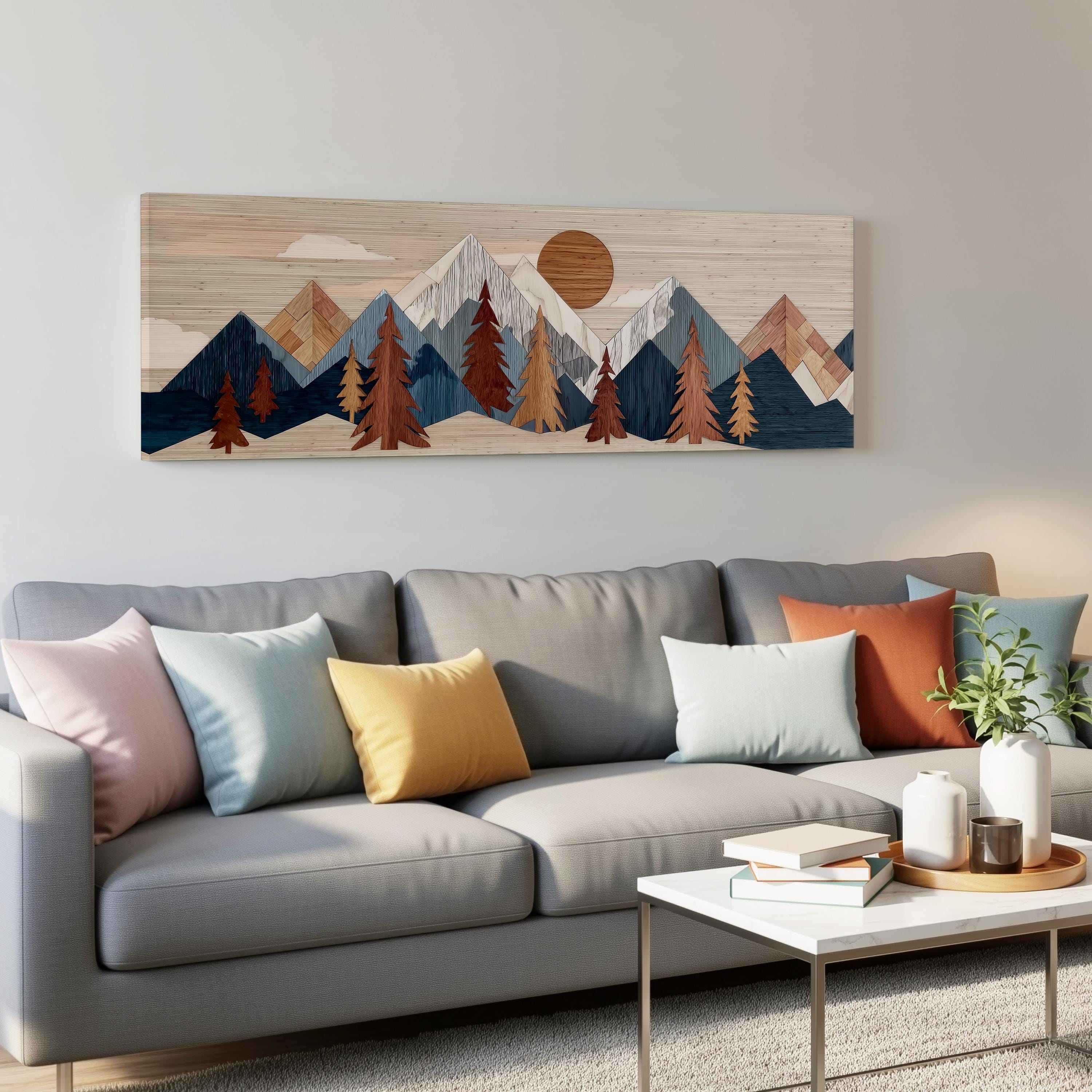a living room with a gray sofa adorned with colorful throw pillows. Above the sofa, there is a large wooden artwork depicting a mountain landscape with a sun in the sky. The artwork is mounted on the wall above a coffee table, which has a stack of books and a small plant on it.