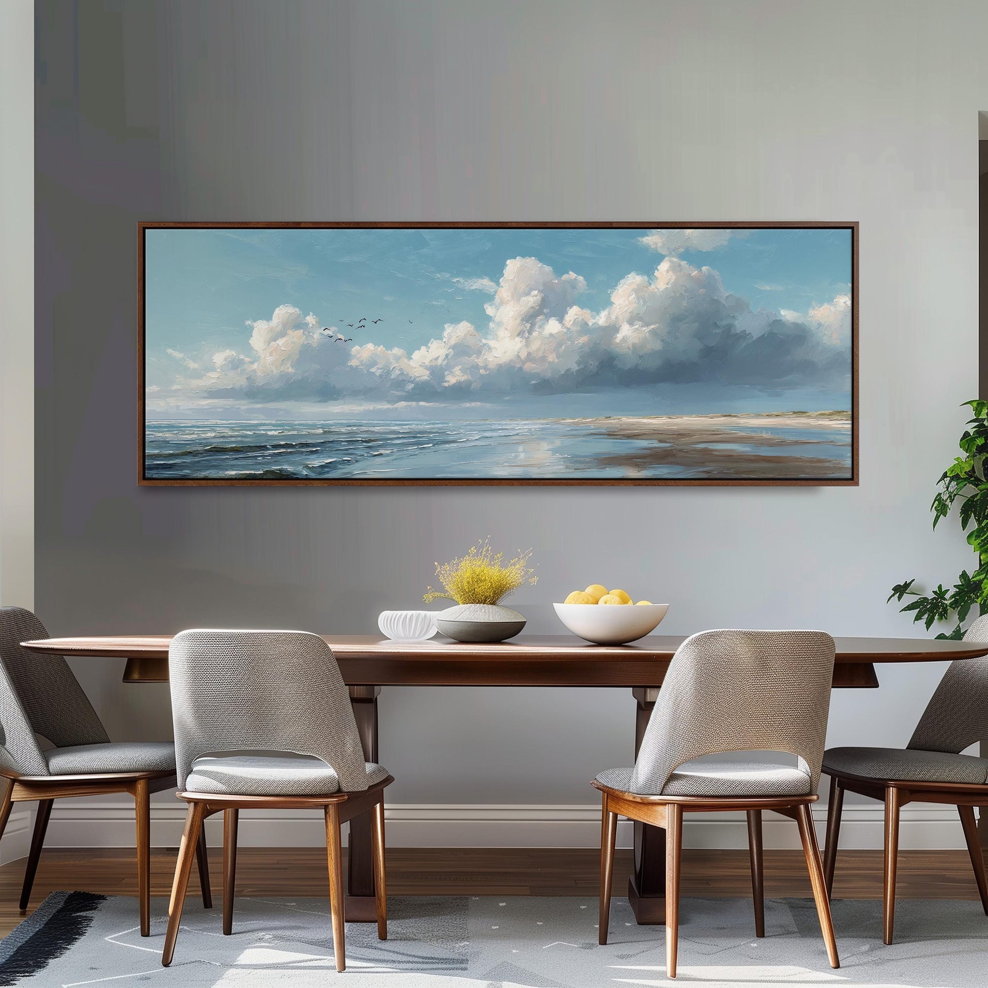a dining room with a large painting of a serene landscape hanging on the wall above a wooden dining table with four chairs. The painting depicts a cloudy sky over a beach, with birds flying in the distance.