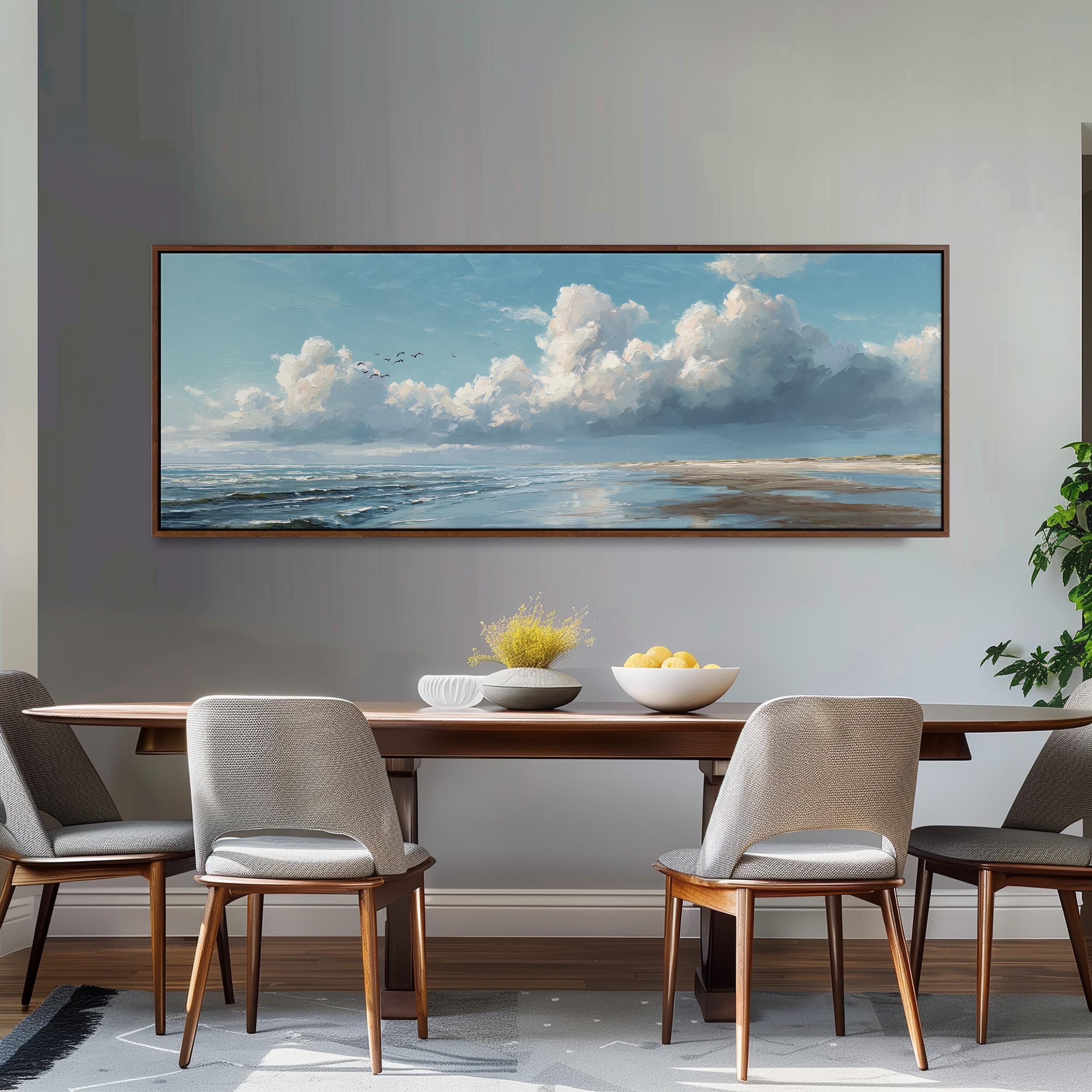 a dining room with a large painting of a serene landscape hanging on the wall above a wooden dining table with four chairs. The painting depicts a cloudy sky over a beach, with birds flying in the distance.