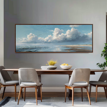 a dining room with a large painting of a serene landscape hanging on the wall above a wooden dining table with four chairs. The painting depicts a cloudy sky over a beach, with birds flying in the distance.